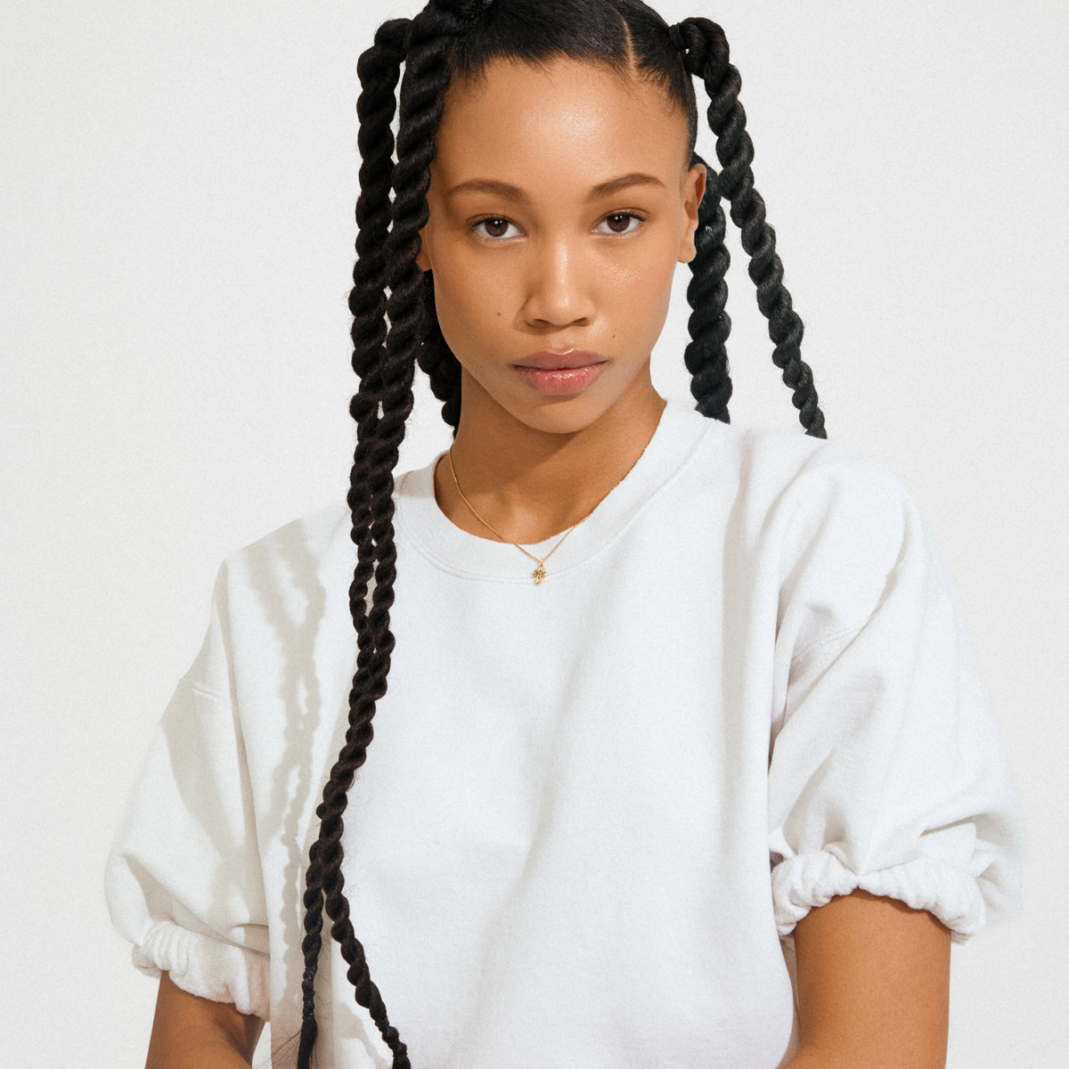 Young woman wearing the DAGMAR mini pendant necklace gold-plated, featuring a mini Dagmar Cross on a delicate chain, styled against a plain background.
