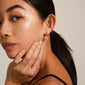 A close-up of a woman wearing Pilgrim's DAGMAR gold-plated huggie hoop earrings with small Dagmar Crosses.