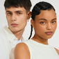 Two young adults wearing DAGMAR huggie hoop earrings with gold-plated Dagmar Cross charms, showcasing Pilgrim's minimalist, modern Danish jewelry design.