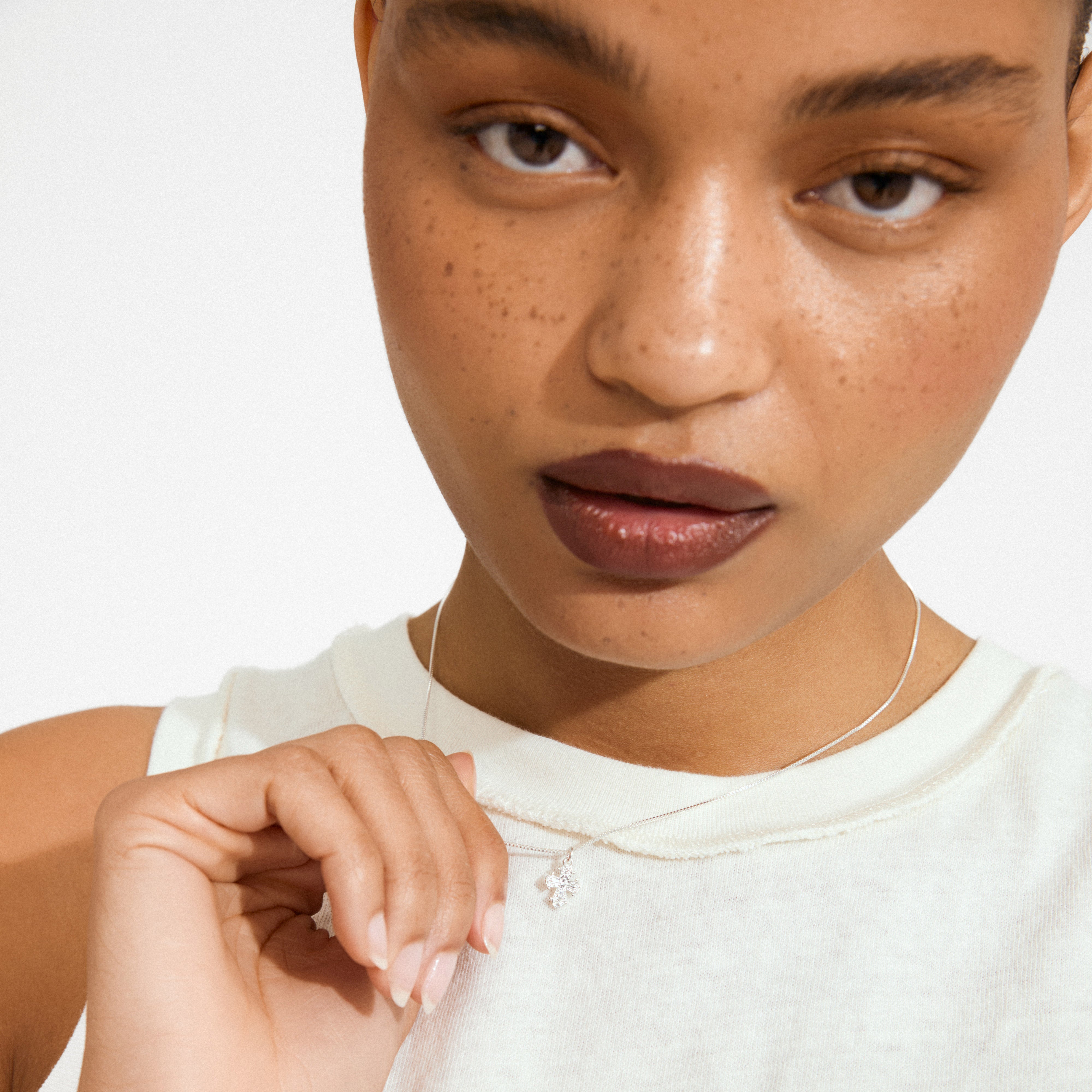Young woman with freckles holding a DAGMAR mini pendant necklace. The silver-plated cross hangs from a delicate chain, embodying Pilgrim's Scandinavian craftsmanship.