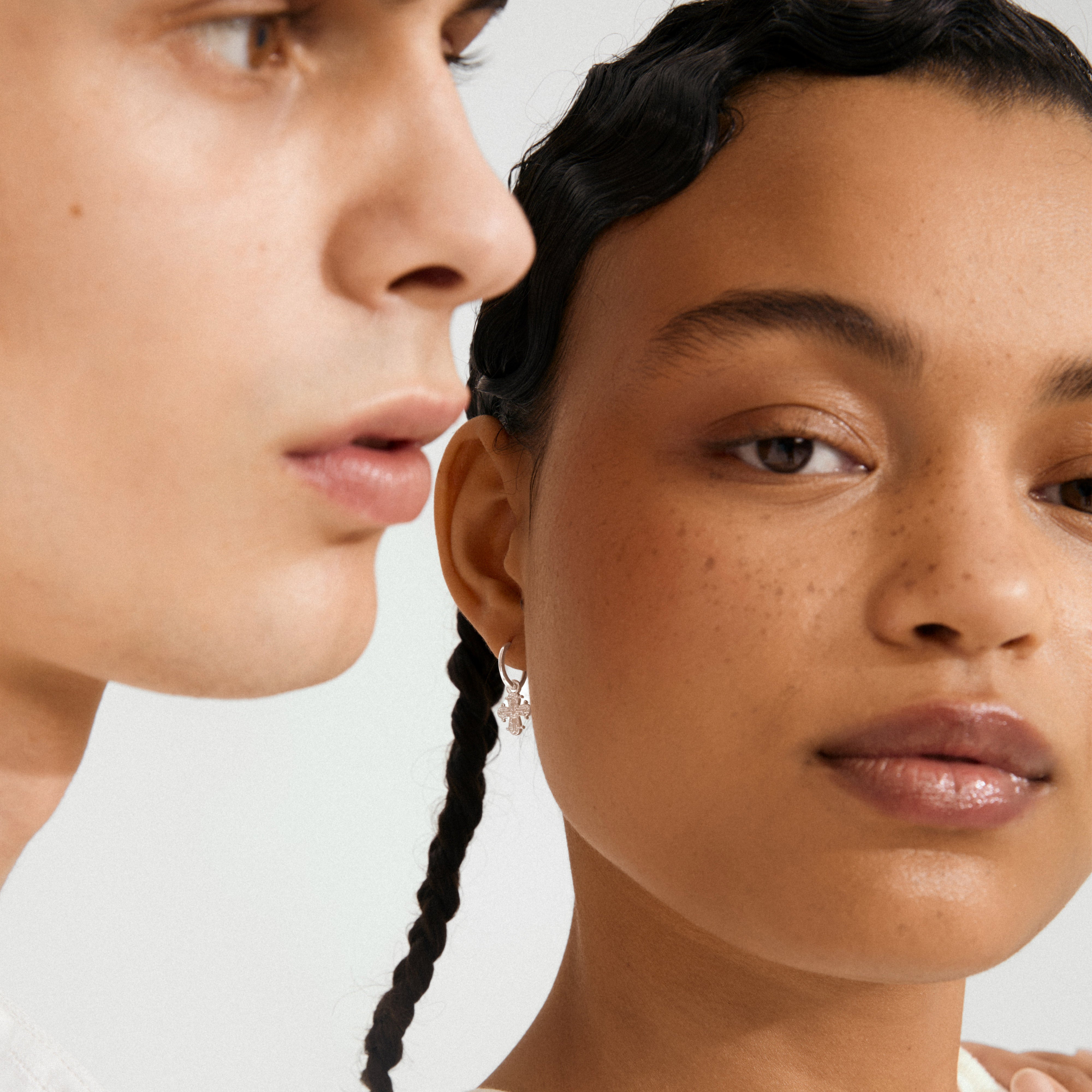 DAGMAR huggie hoop earrings silver-plated, worn by a woman with braided hair, featuring a delicate, dangling Dagmar Cross charm, highlighting Scandinavian elegance and recycled craftsmanship.
