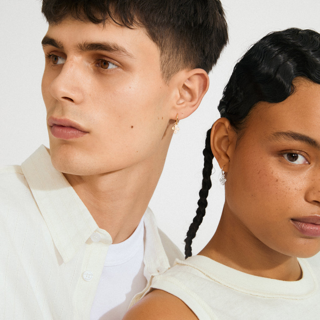 Two young models showcase DAGMAR huggie hoop earrings. Silver-plated, with mini Dagmar Crosses, offering a stylish, updated Danish classic from Pilgrim.