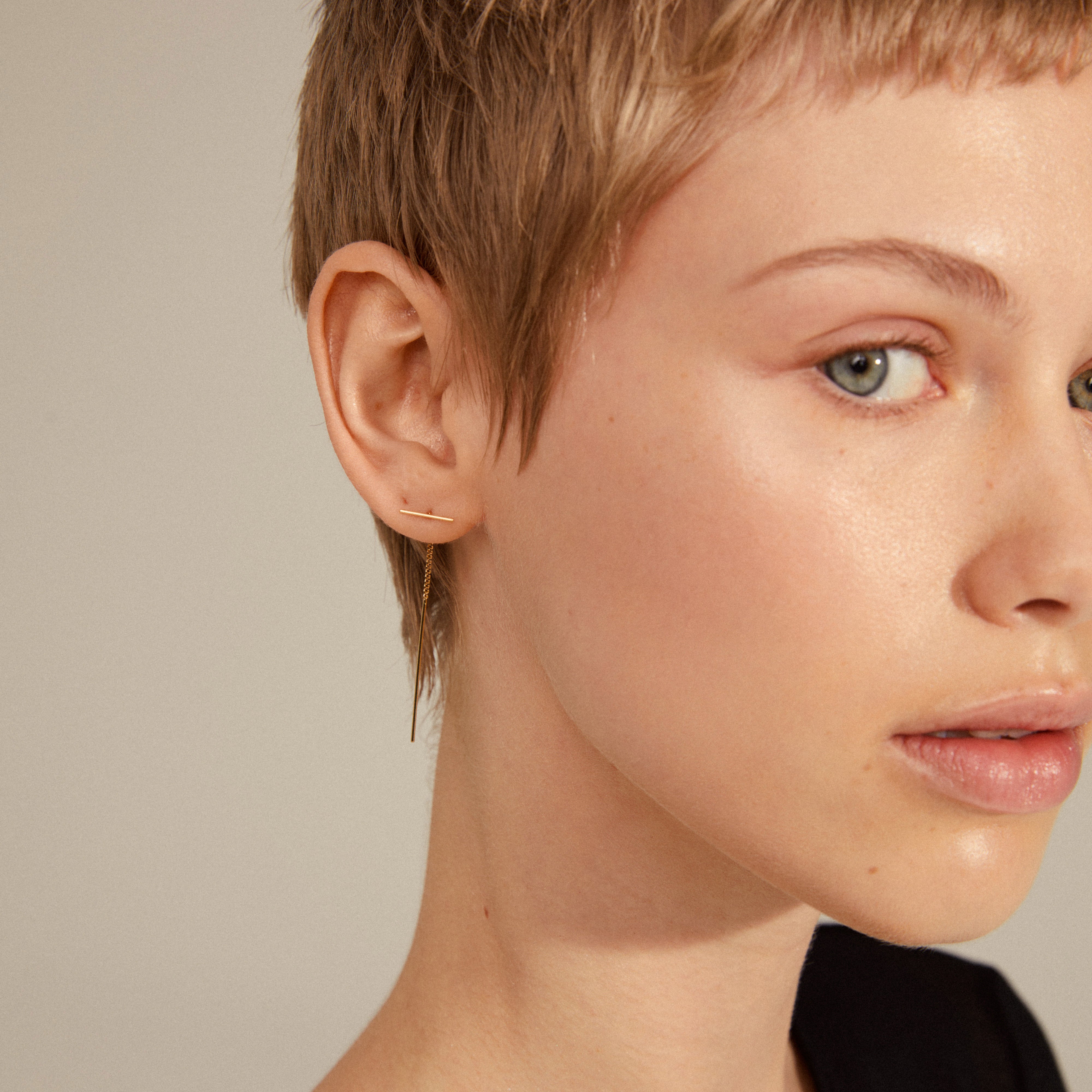 BRIELLE gold-plated earrings on a woman with short hair, featuring a minimalist transverse bar and delicate chain for a stylish, versatile look.