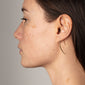 Profile of a woman wearing AGATHA earrings, gold-plated with a delicate curve, accentuating her neckline. Timeless design, perfect for enhancing trendy, personal styles.