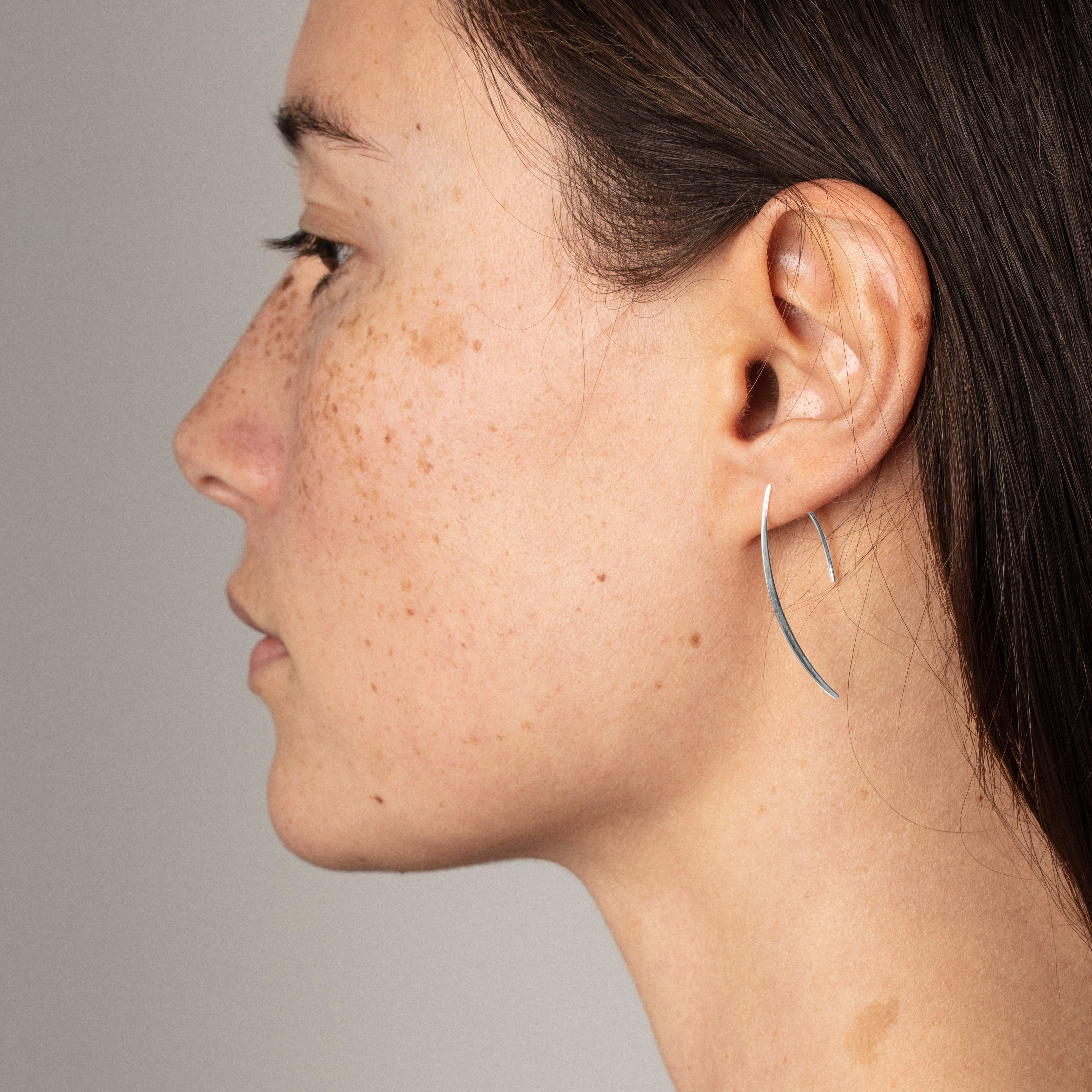 Side view of a woman wearing AGATHA silver-plated earrings, elegantly dangling to a thin line, embodying Pilgrim's blend of classic and edgy style.