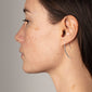 Side view of a woman wearing AGATHA silver-plated earrings, elegantly dangling to a thin line, embodying Pilgrim's blend of classic and edgy style.