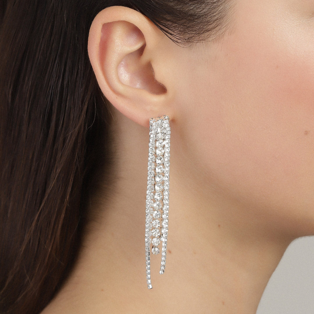 Close-up of RACHEL earrings, silver-plated, with cascading, sparkling crystals hanging elegantly from a woman's ear, capturing light like a shimmering waterfall.