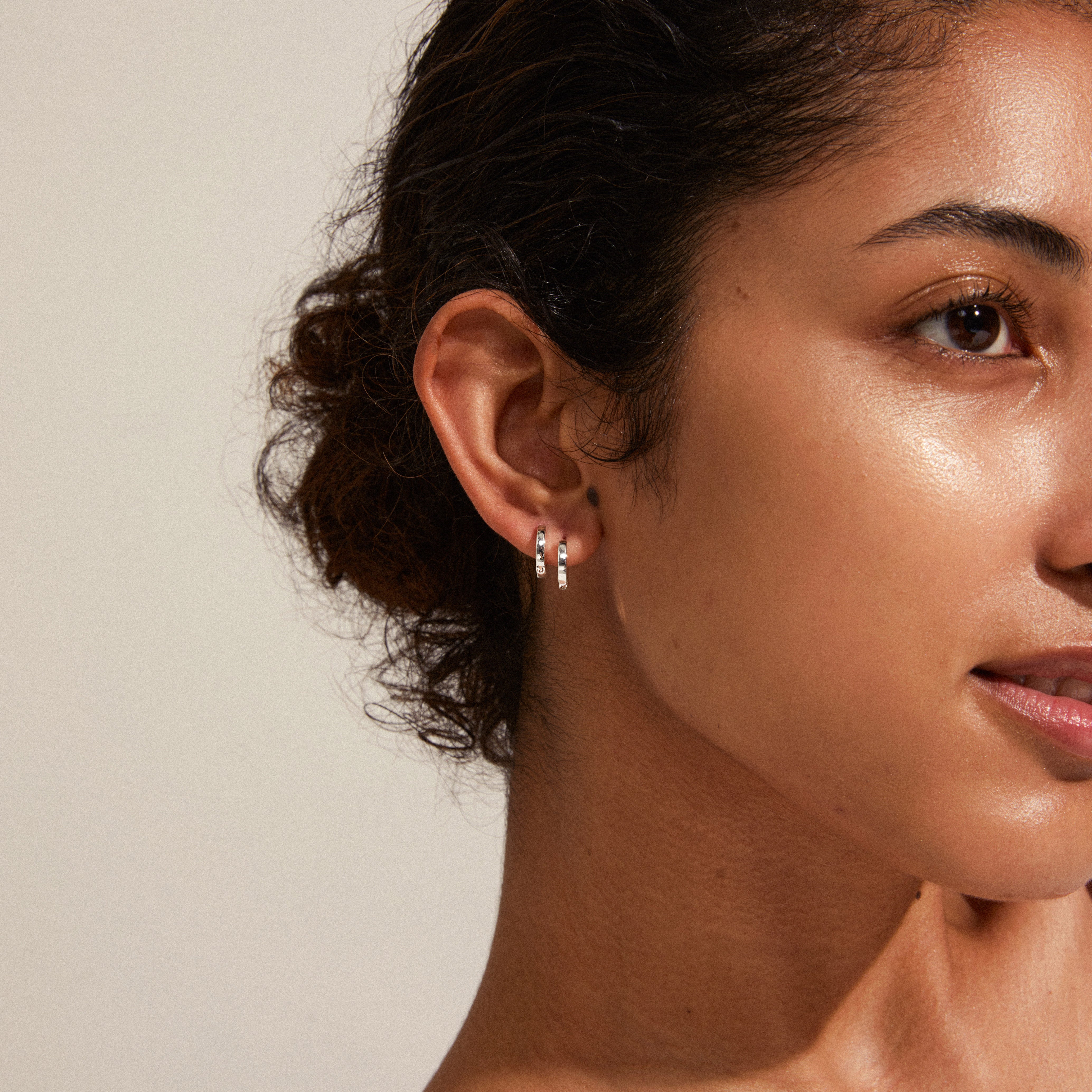 ARNELLE silver-plated huggie hoop earrings showcased on a woman with dark hair, highlighting their polished finish and elegant design.