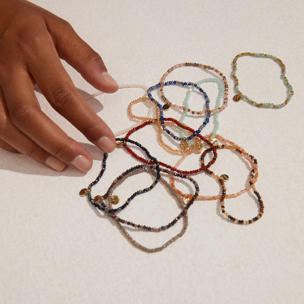 A hand holds the INDIE bracelet, showcasing its sparkling dark blue beads and discreet gold-plated Pilgrim logo, exemplifying Scandinavian craftsmanship.