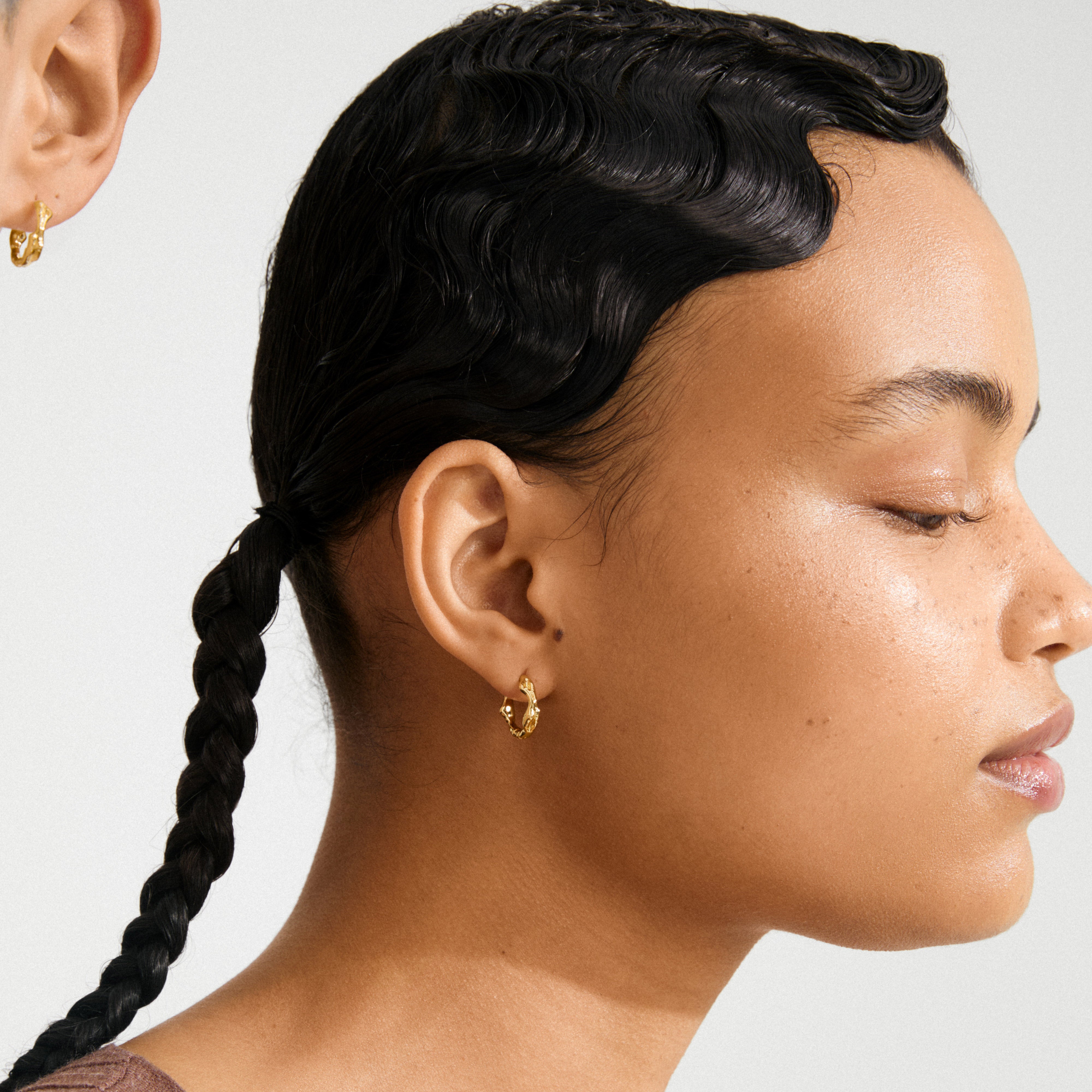 Profile view showcasing the ZION small huggie hoop earrings in gold-plated finish, highlighting their textured, quirky design on a person with finger wave hairstyle.