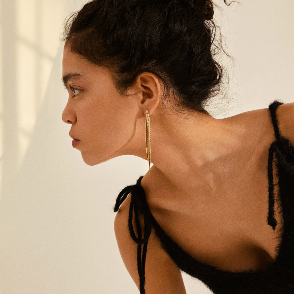 Young woman wearing CARMEN waterfall earrings gold-plated, featuring long, delicate chains that exude feminine elegance, paired with a black fuzzy tank top.