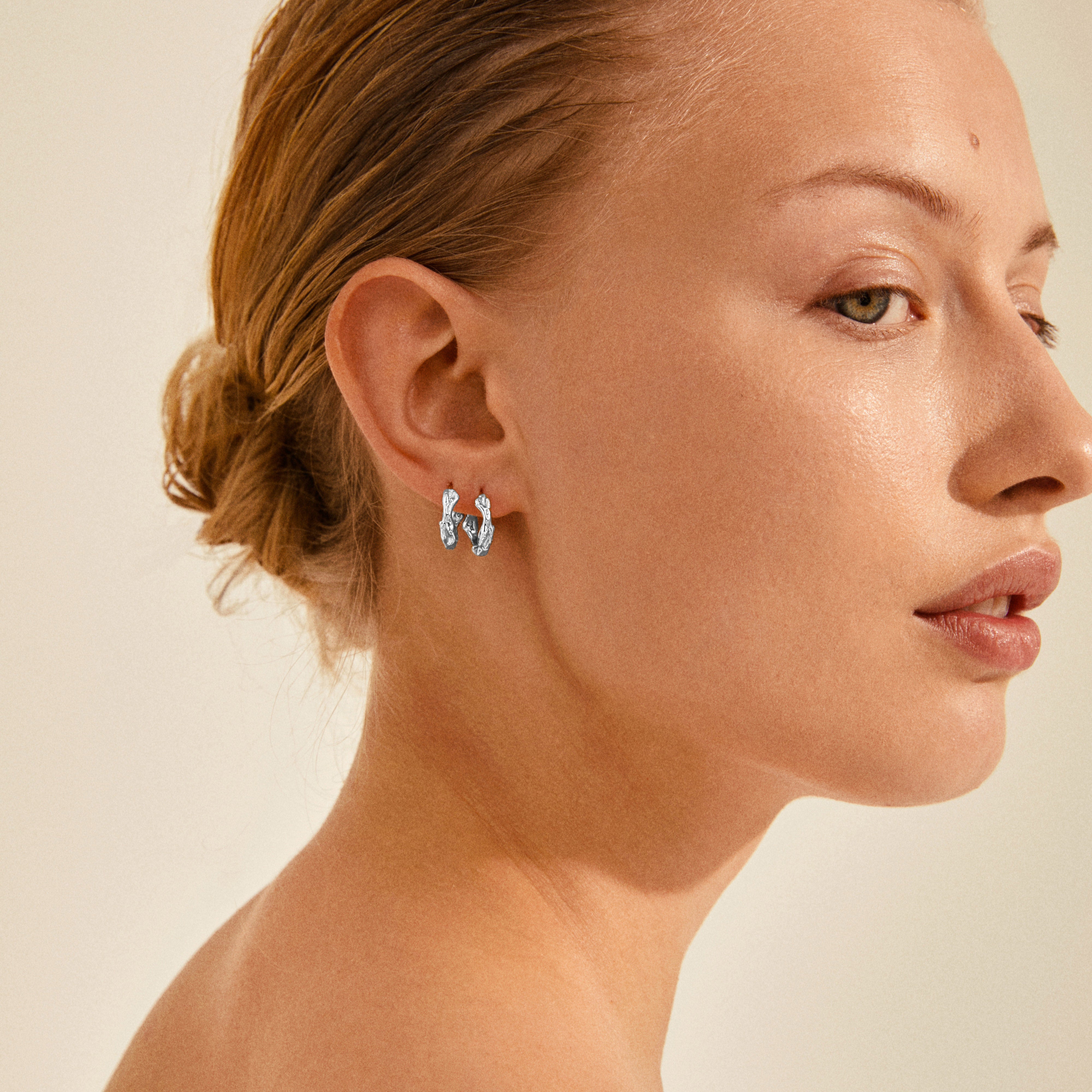 Woman wearing ZION small huggie hoop earrings, silver-plated, showcasing their playful, classy design. Perfect for adding a creative touch to any outfit.