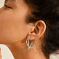 MILLER graphic statement earrings silver-plated feature sculptural, fluid curves, shown elegantly hanging from an ear with dark hair pulled back.