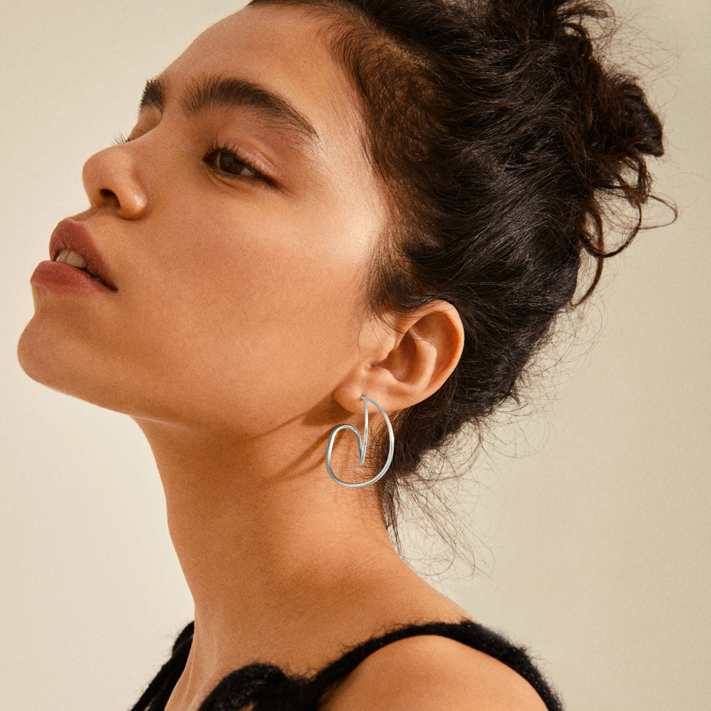 Young woman wearing MILLER graphic statement earrings silver-plated, featuring elegant, drop-shaped design, highlighting Pilgrim's blend of timeless and trendy Scandinavian craftsmanship.