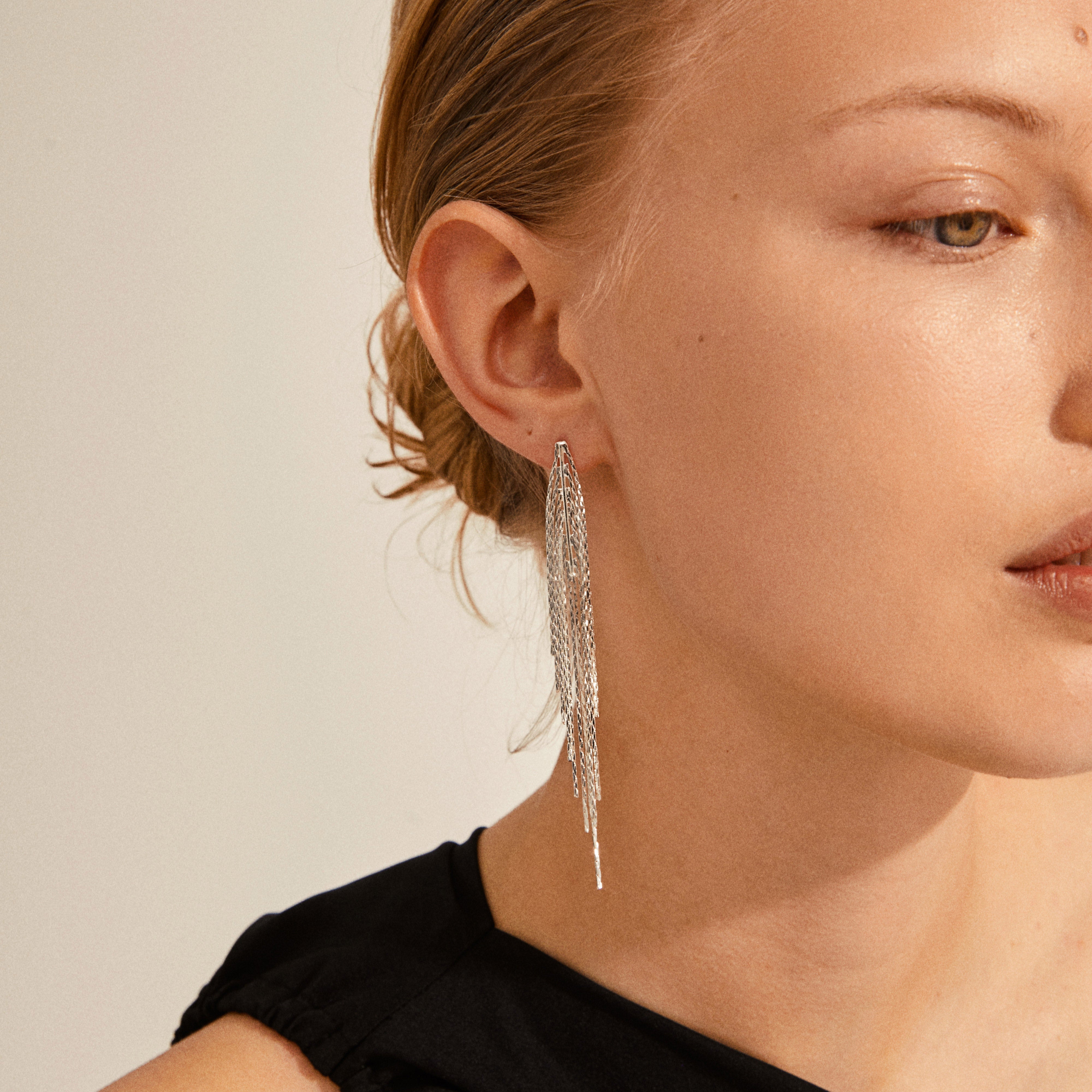 Woman wearing CARMEN waterfall earrings, silver-plated with long chain tassels, styled with a simple black top and hair pulled back.