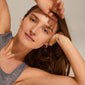 Woman wearing PIA organic shape crystal hoop earrings, showcasing gold-plated, wavy design with Preciosa crystals for an elegant, natural look.
