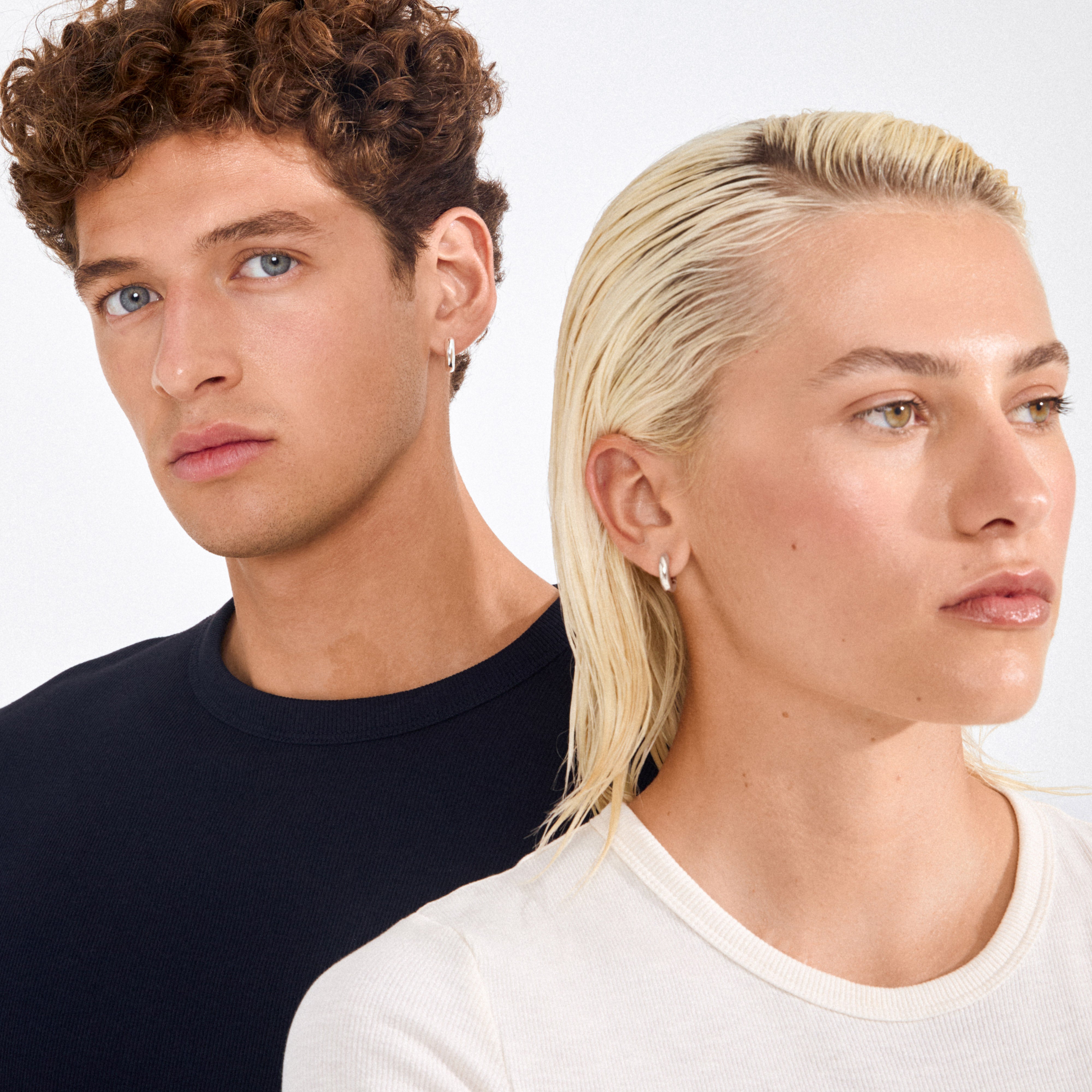 Two young adults wearing Pilgrim's AICA chunky huggie hoop earrings, showcasing the bold, minimalist design of the silver-plated accessory.