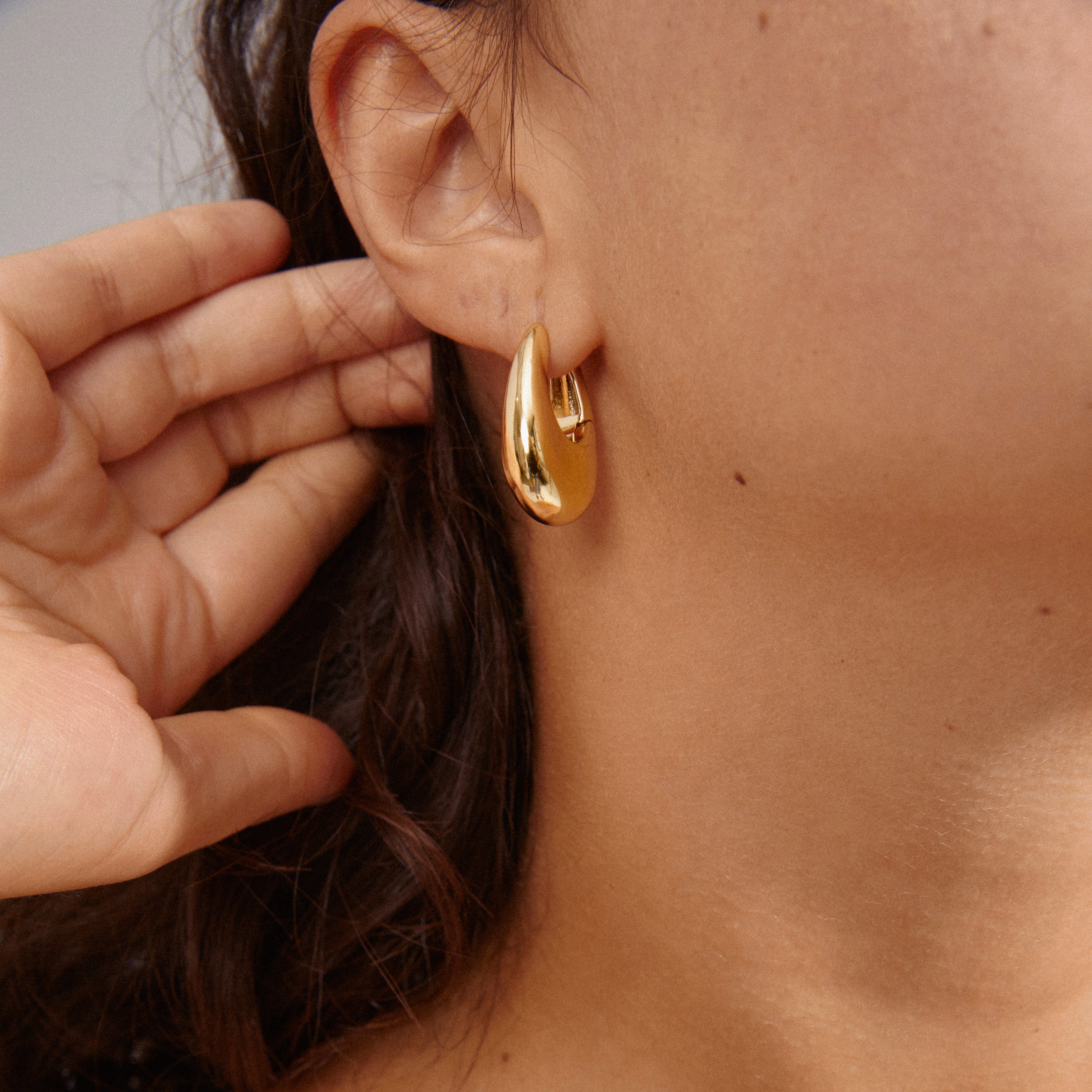 Close-up of a woman's ear showcasing gold-plated AUTUMN chunky retro hoop earrings with a teardrop design, highlighting their bold, vintage-inspired look from Pilgrim.