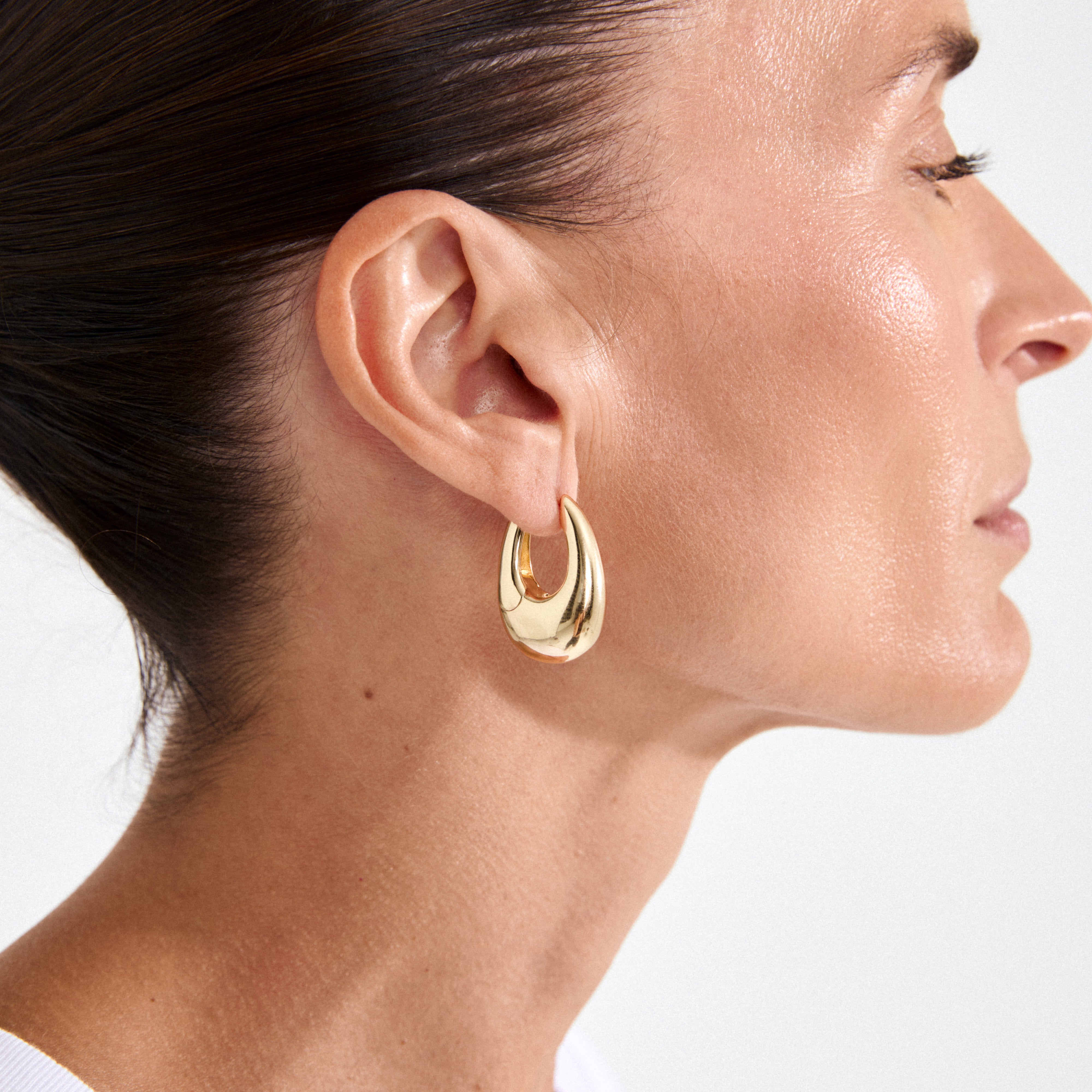 Woman wearing AUTUMN chunky retro hoop earrings, gold-plated, featuring a teardrop shape that adds a classy, bold touch to her look.