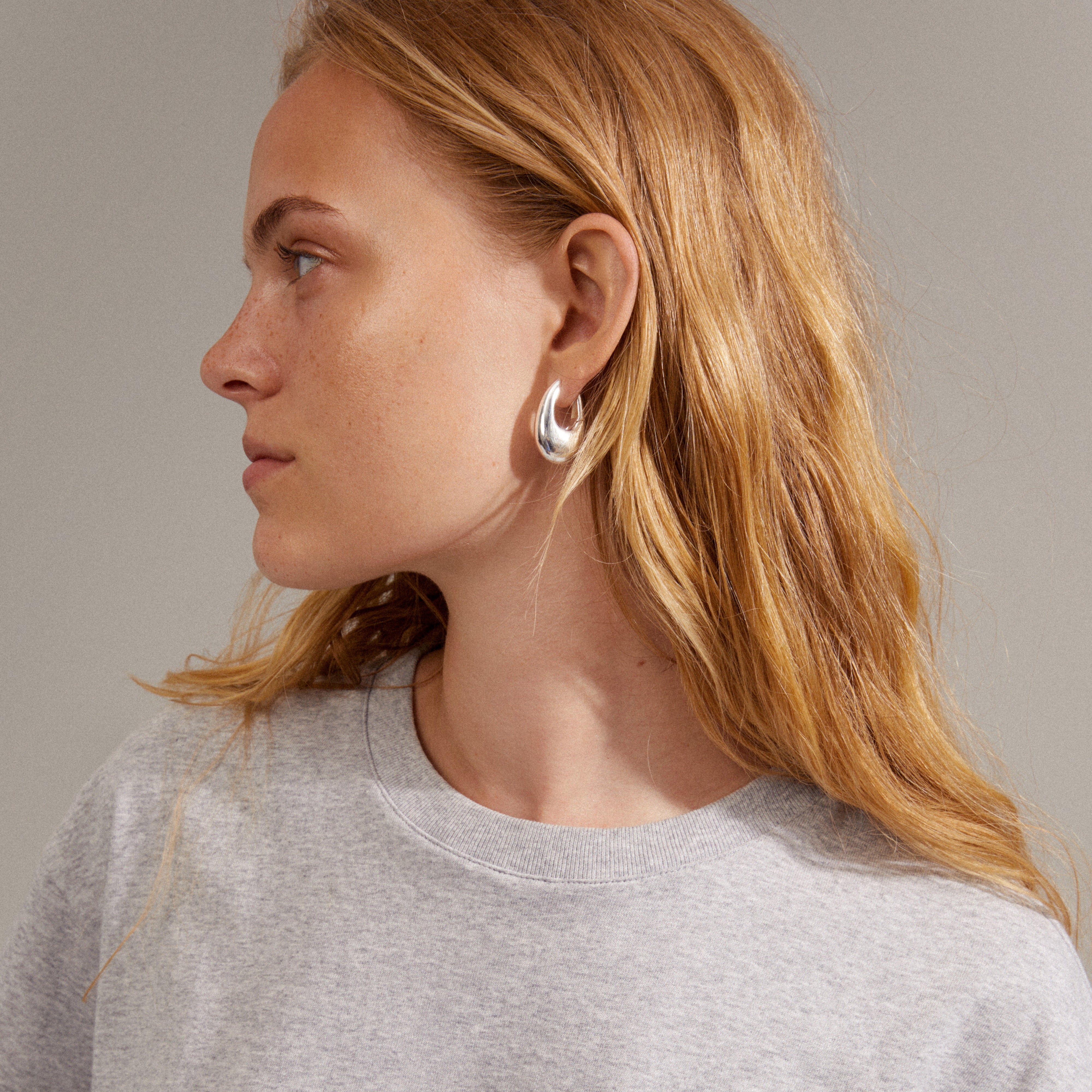 Close-up of a woman wearing AUTUMN chunky retro hoop earrings, silver-plated, highlighting their teardrop design and robust, chunky look.