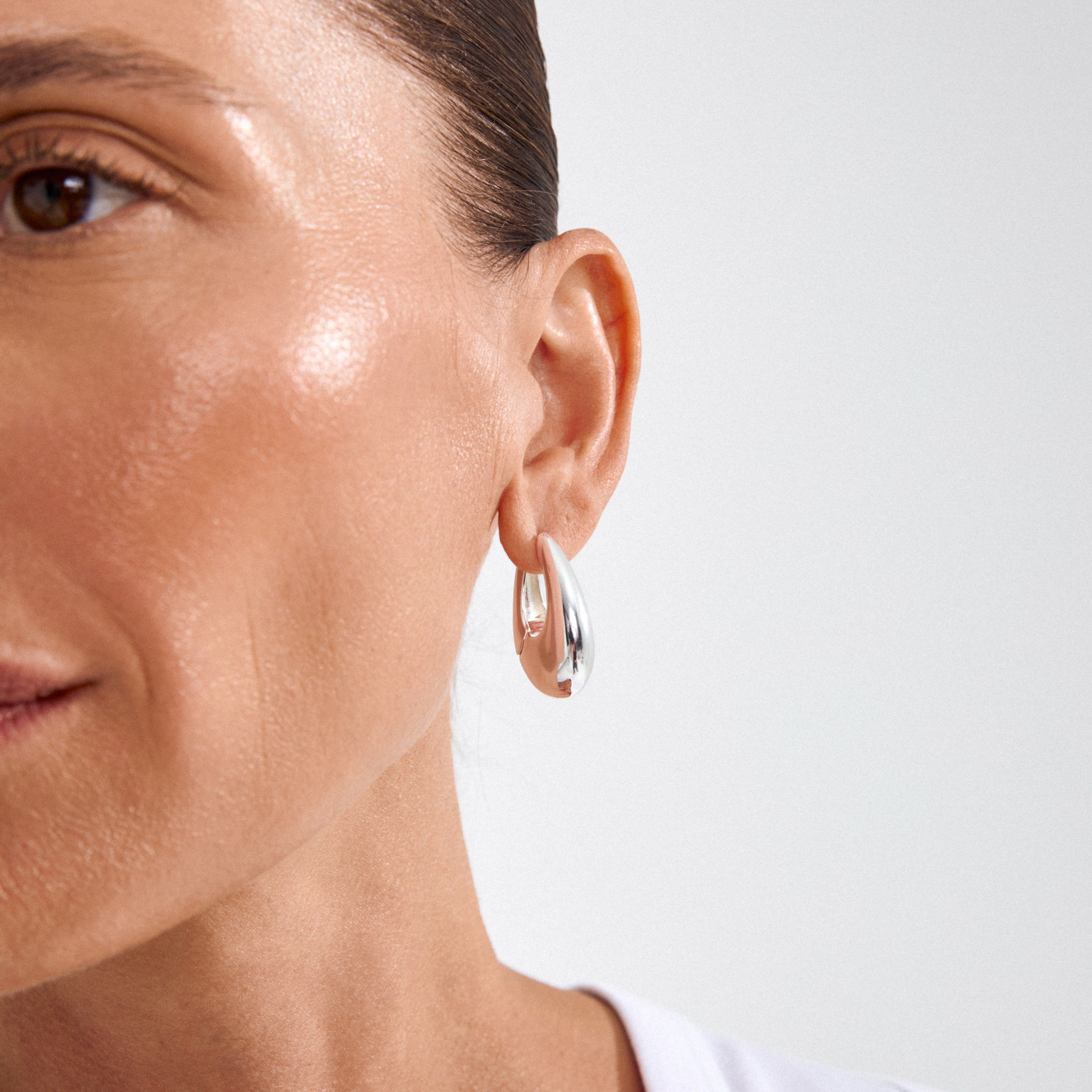 Close-up of the AUTUMN chunky retro hoop earrings in silver-plated teardrop design, worn on a person's ear, showcasing their bold, statement-making style.