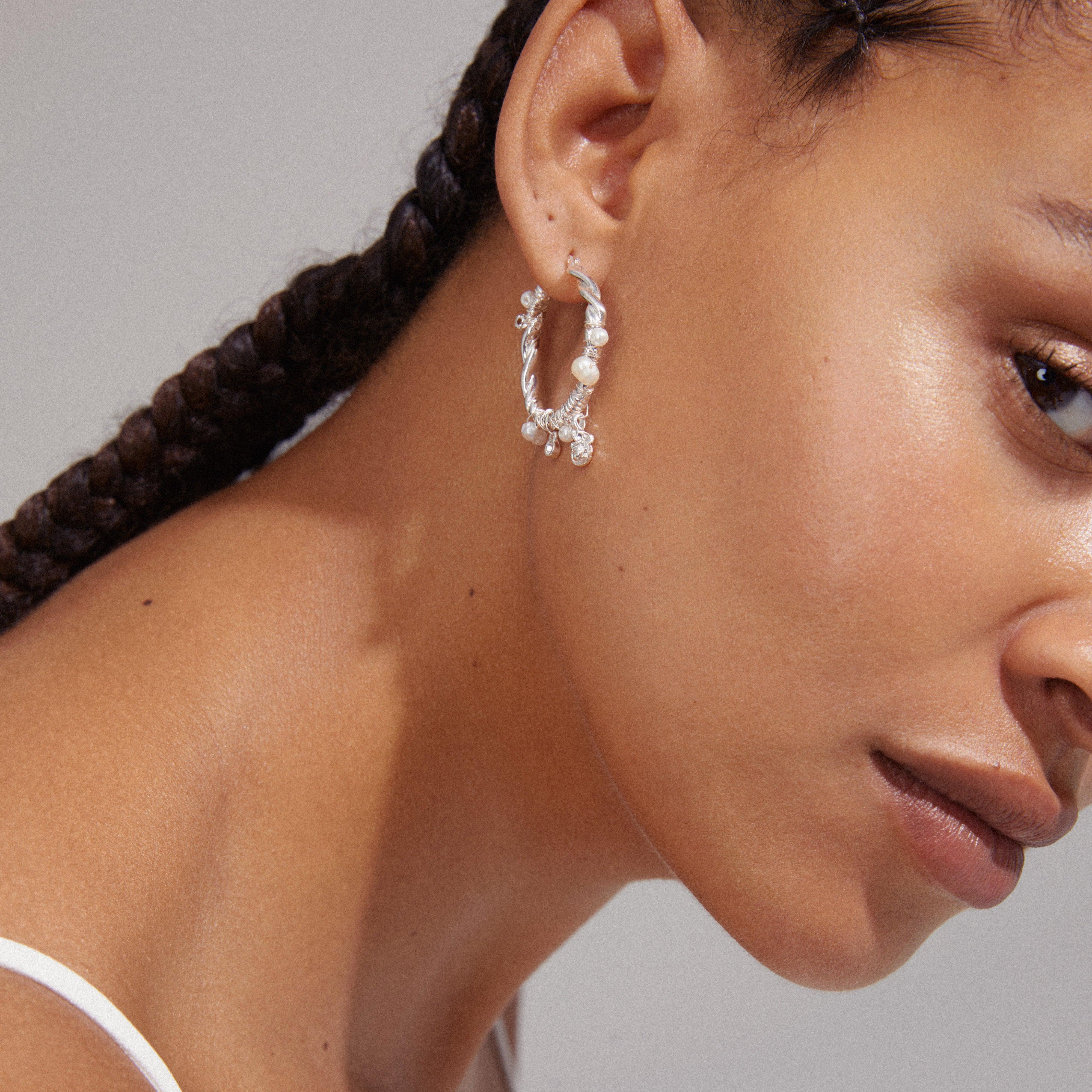 Silver-plated ANA hoops with freshwater pearls and Preciosa crystals, featuring a twisted design, worn by a woman with braids and earrings.