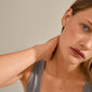 Woman wearing OCTAVIA clover earrings, gold-plated, touching her neck. The earrings feature a four-leaf clover design, symbolizing luck and positivity.