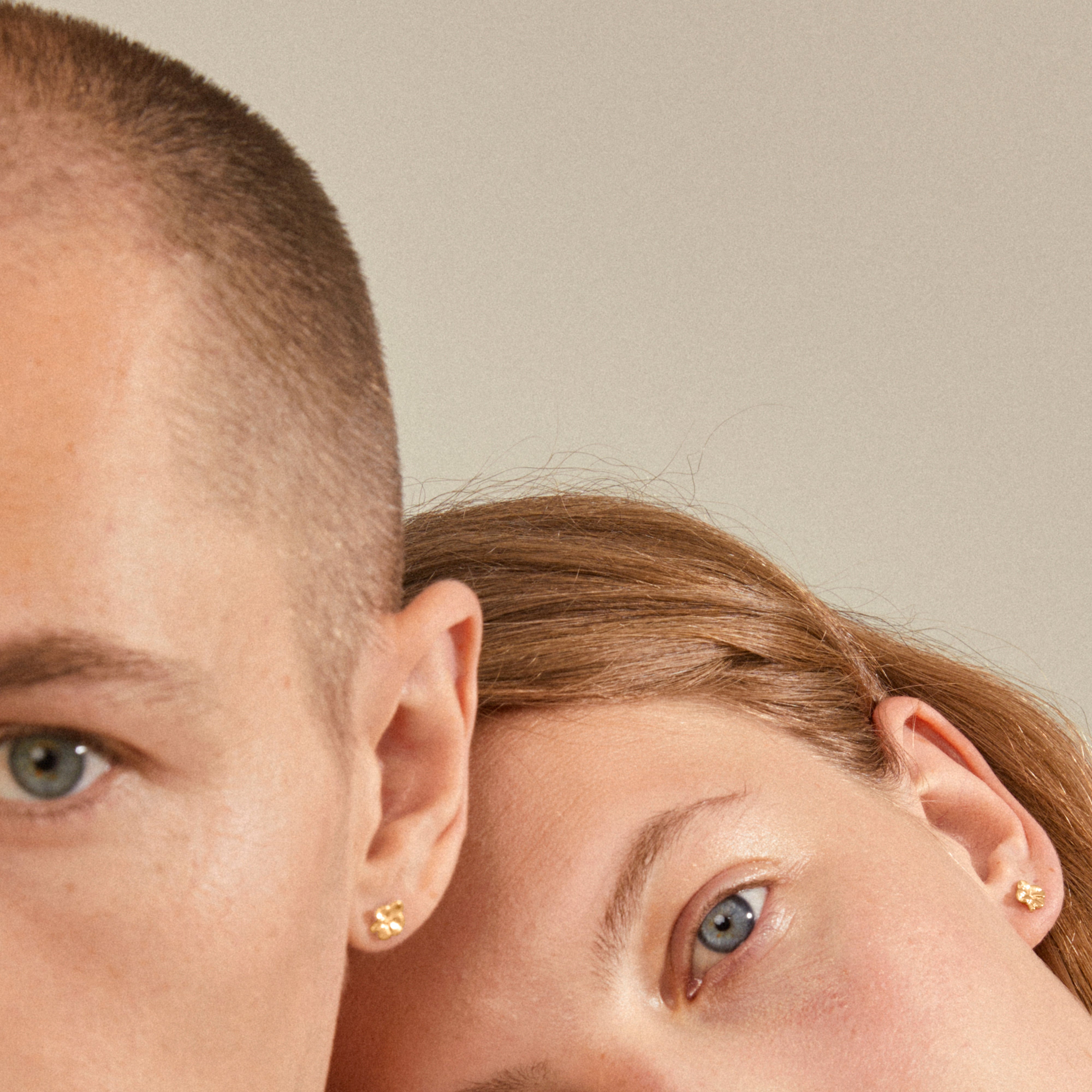 Two faces with OCTAVIA clover earrings, gold-plated, showcasing minimalist elegance. These recycled, lucky charm studs accentuate a modern, everyday style.