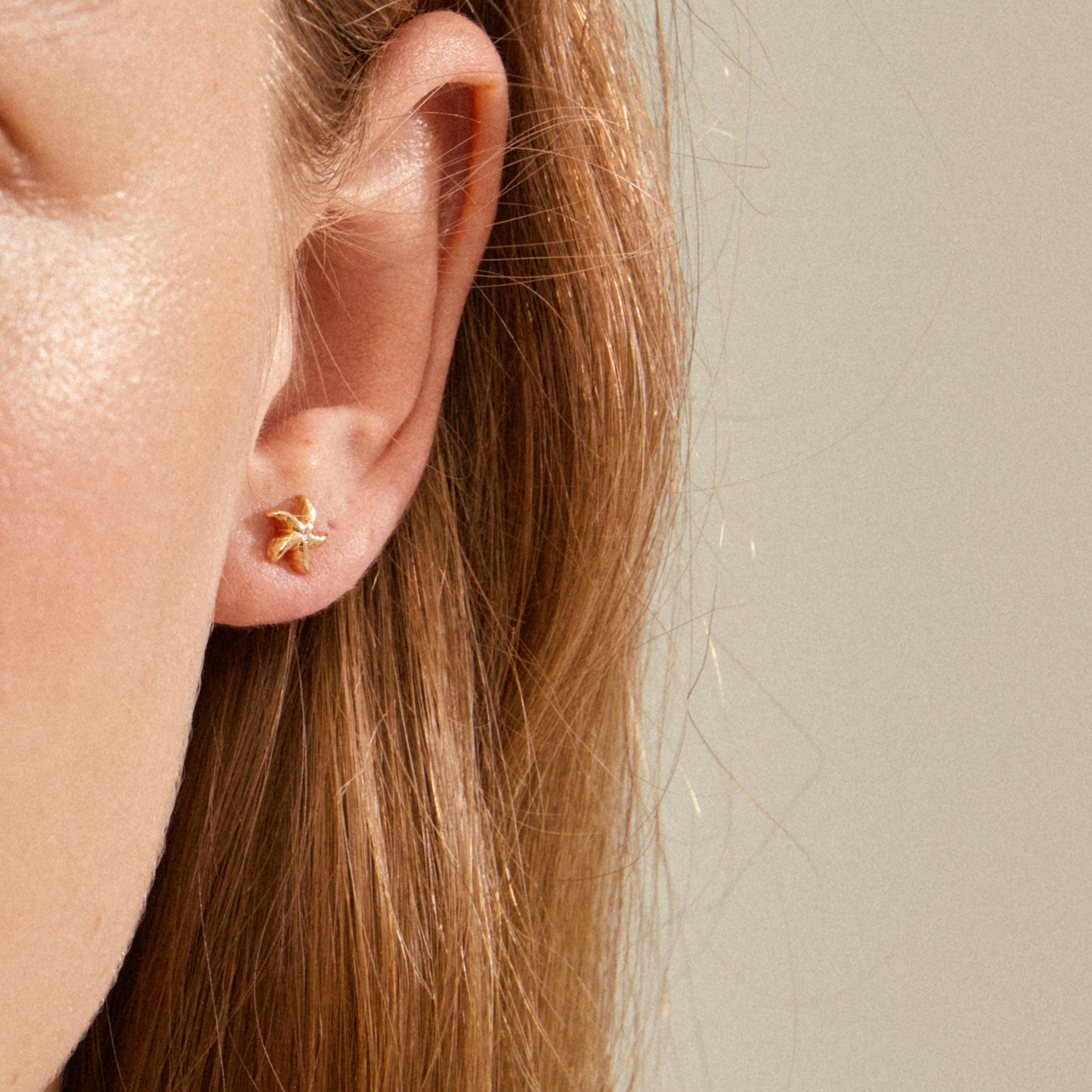 Gold-plated OAKLEY starfish earring on a person's earlobe, showcasing its small, elegant design ideal for mixing and matching with other jewelry.