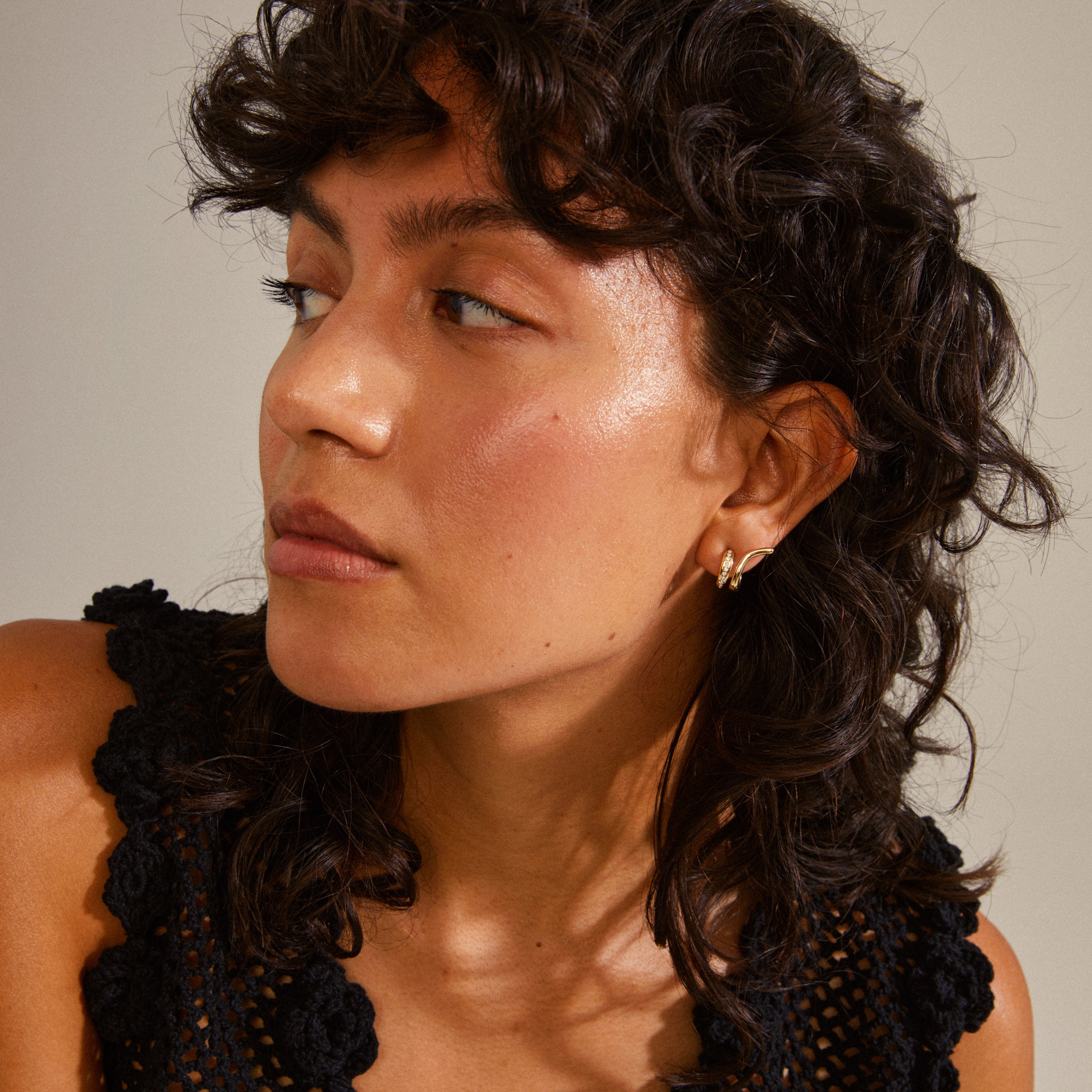 Close-up of a woman wearing gold-plated NADINE earrings by Pilgrim, featuring tiny Preciosa crystals and a stylish ear crawler design.