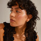 Close-up of a woman wearing gold-plated NADINE earrings by Pilgrim, featuring tiny Preciosa crystals and a stylish ear crawler design.