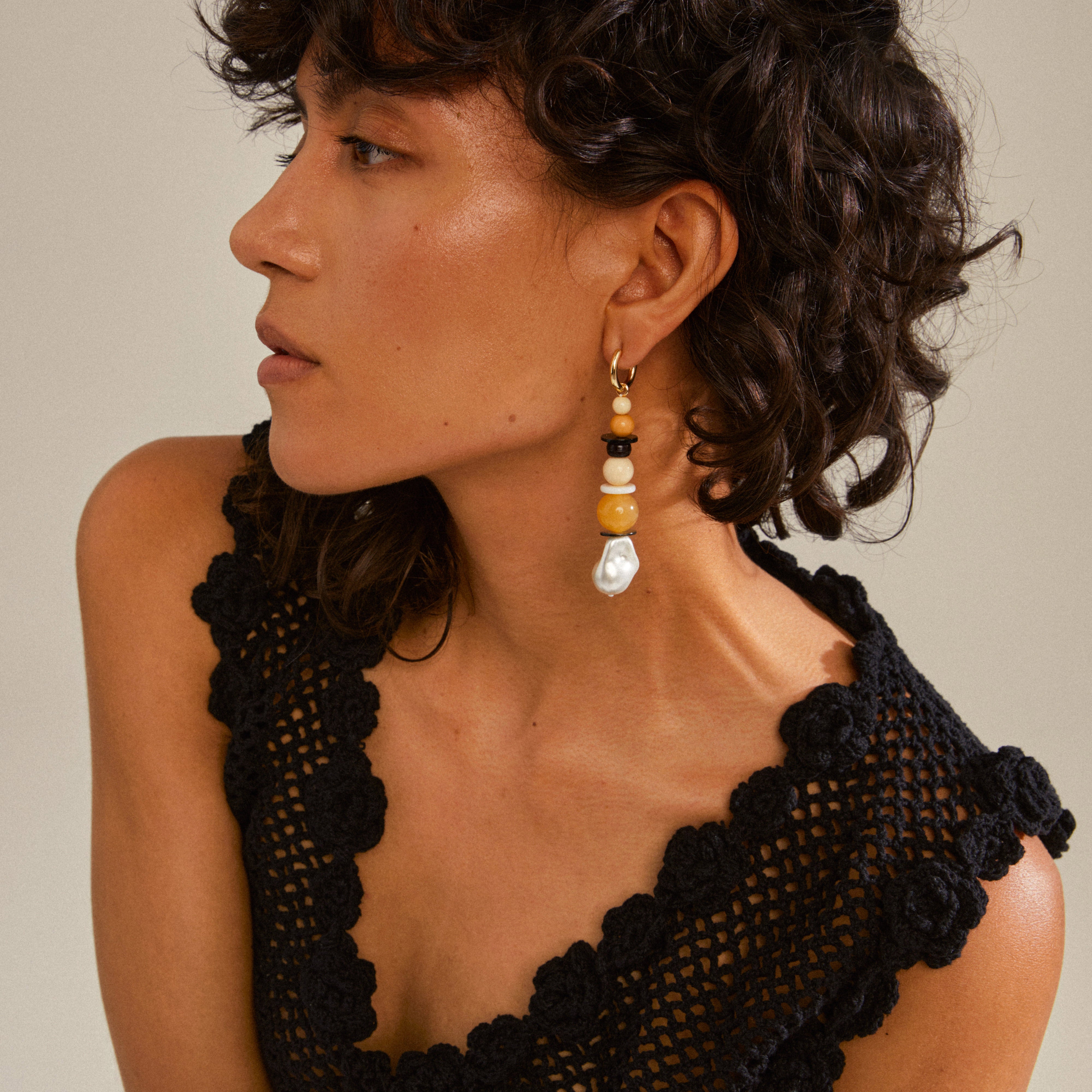 Woman wearing NAILA earrings by Pilgrim; gold-plated hoops with multi-coloured beads, enhancing her black dress for a trendy, eye-catching look.