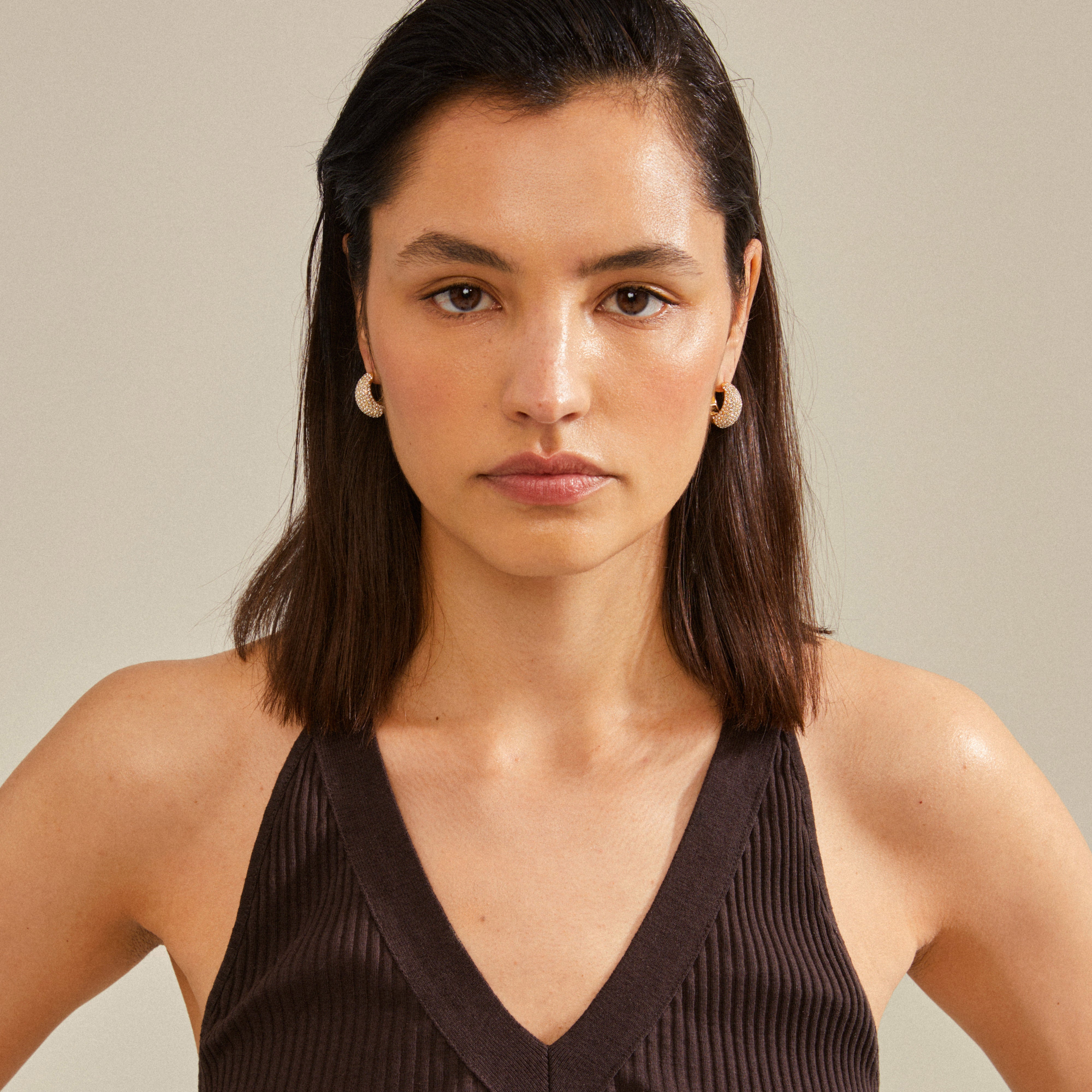 Woman wearing black tank top showcasing NAOMI crystal hoops, gold-plated, from Pilgrim. Hoops feature chunky design with Preciosa crystals, emphasizing sustainability and style.