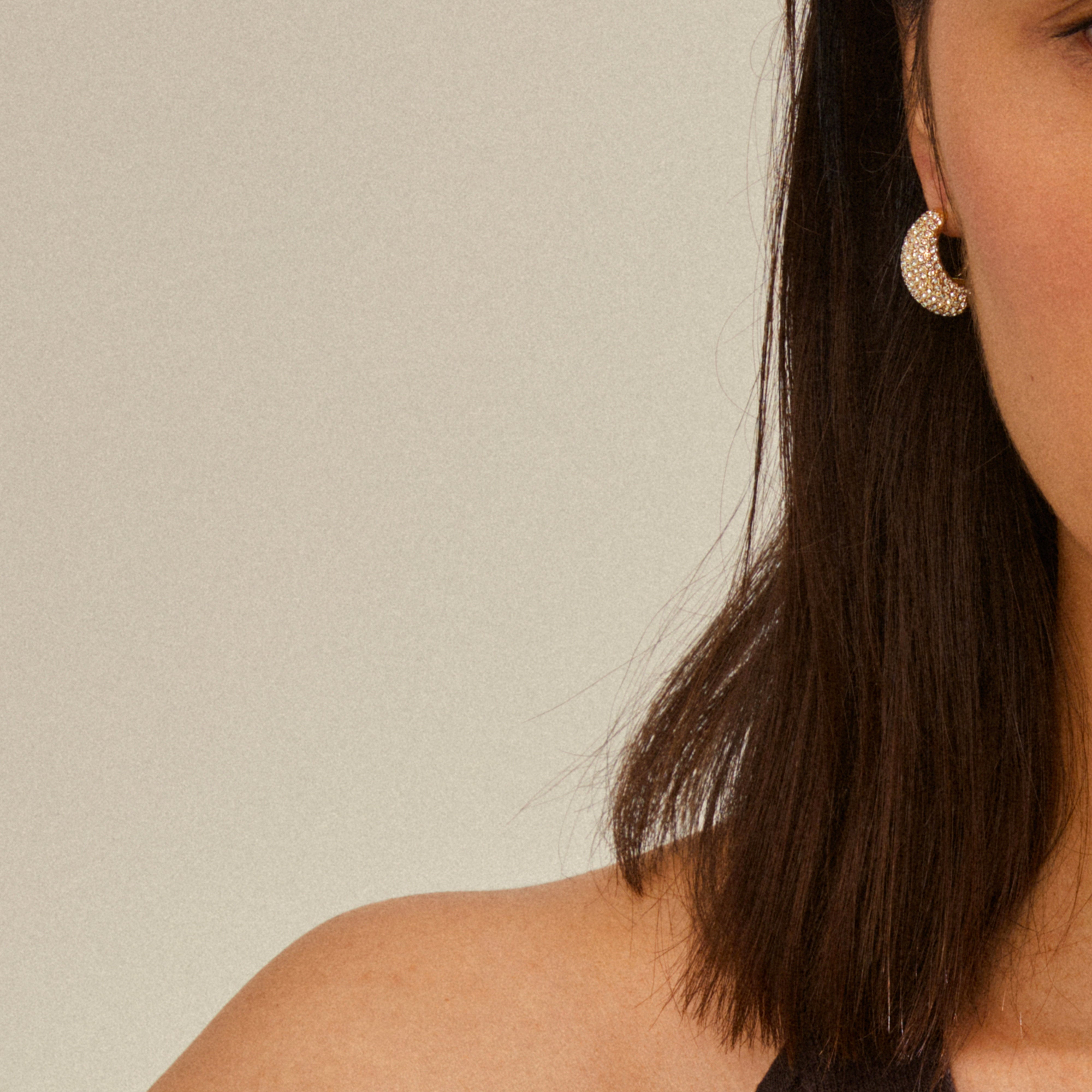 Woman's profile wearing Pilgrim's NAOMI crystal hoops, gold-plated and sparkly, with chunky design showcasing Preciosa crystals against a neutral backdrop.