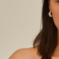 Woman's profile wearing Pilgrim's NAOMI crystal hoops, gold-plated and sparkly, with chunky design showcasing Preciosa crystals against a neutral backdrop.