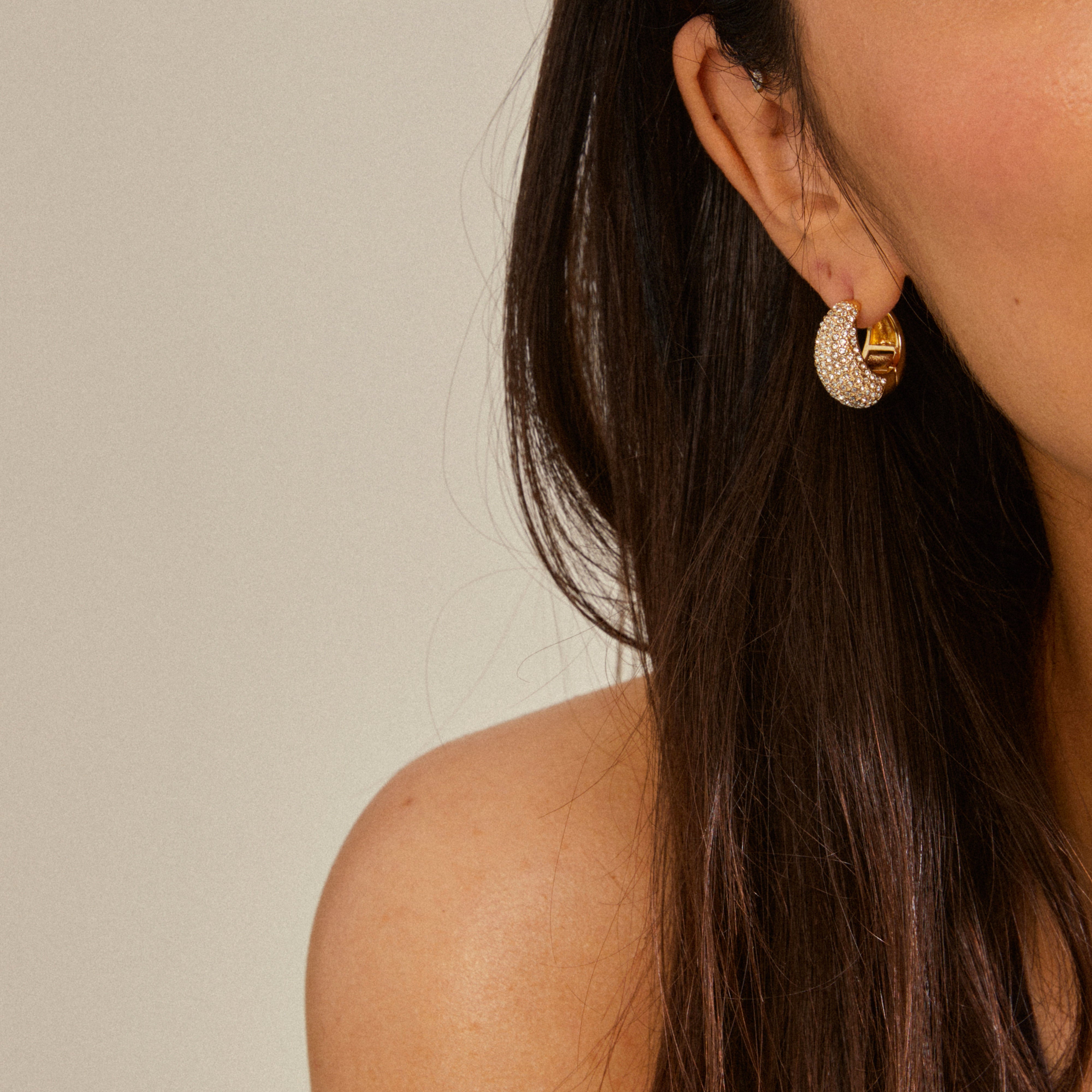 NAOMI crystal hoops gold-plated, featuring chunky half-hoops with sparkling Preciosa crystals, worn by a woman with dark hair, showcasing sophisticated, eco-friendly Pilgrim jewelry.
