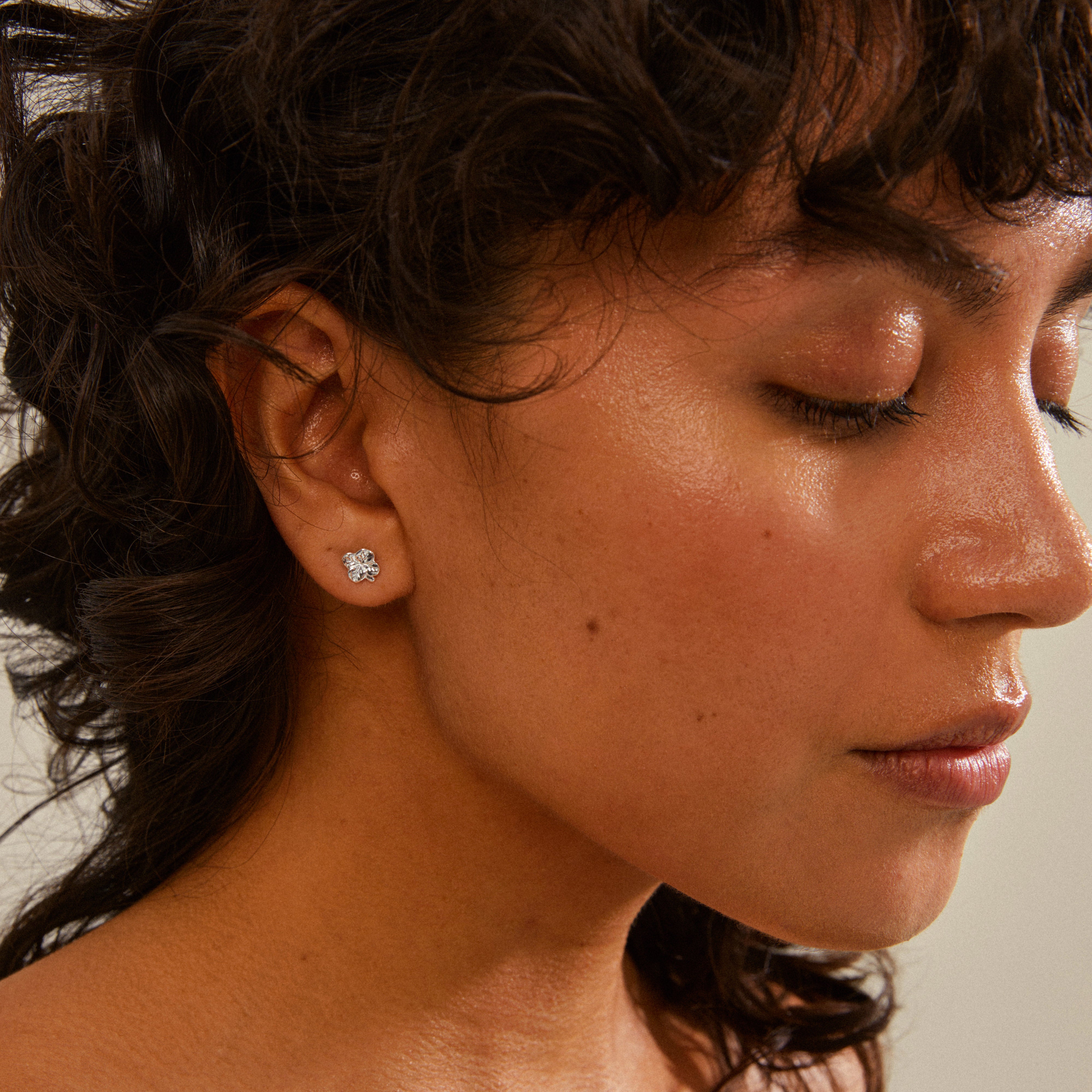 OCTAVIA clover earrings silver-plated on a woman's ear, eyes closed, showcasing the timeless four-leaf clover design symbolizing luck and positivity.