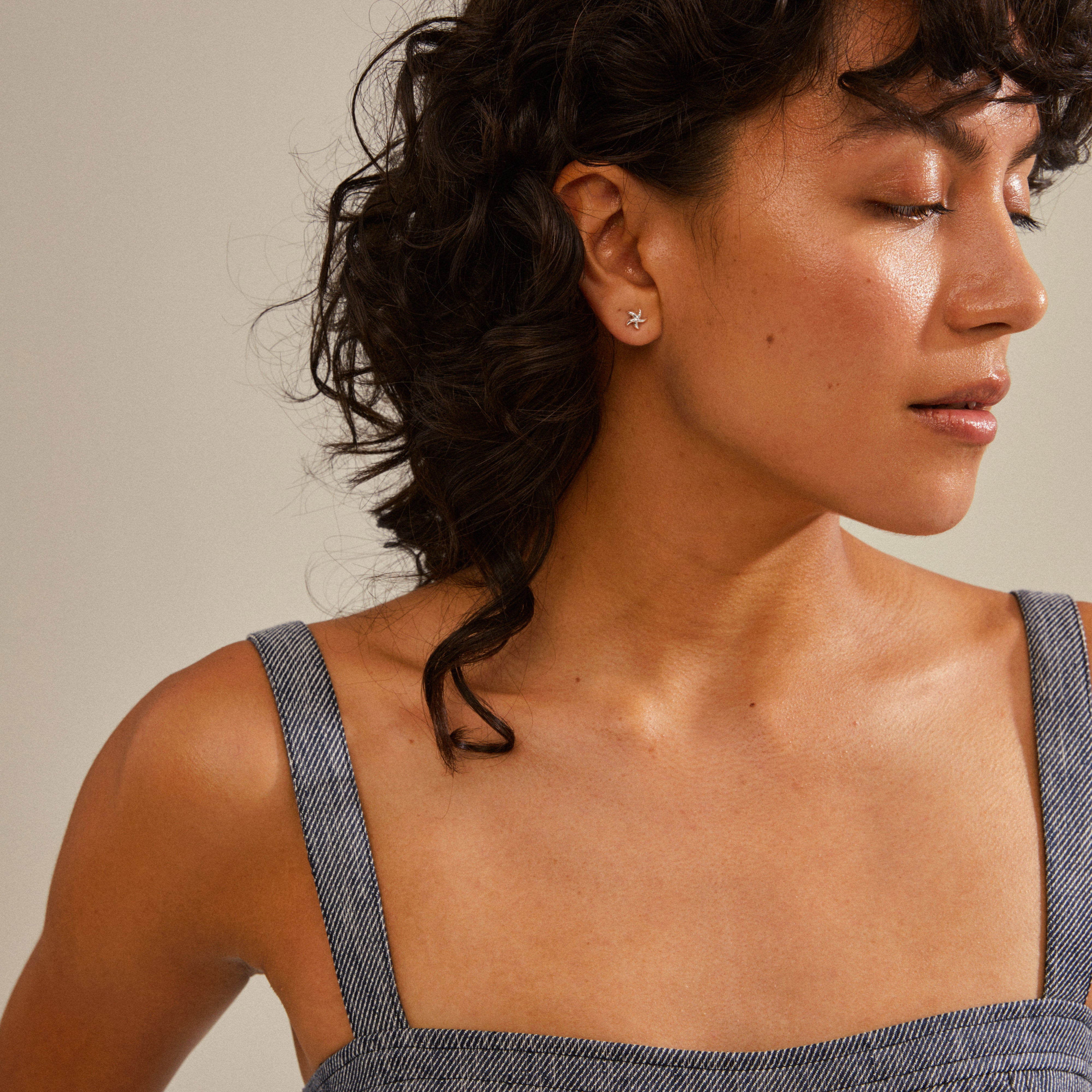 Woman with closed eyes wearing OAKLEY silver-plated starfish earrings, showcasing their discreet, elegant design inspired by ocean life. Ideal for trendy, personalized ear curation.