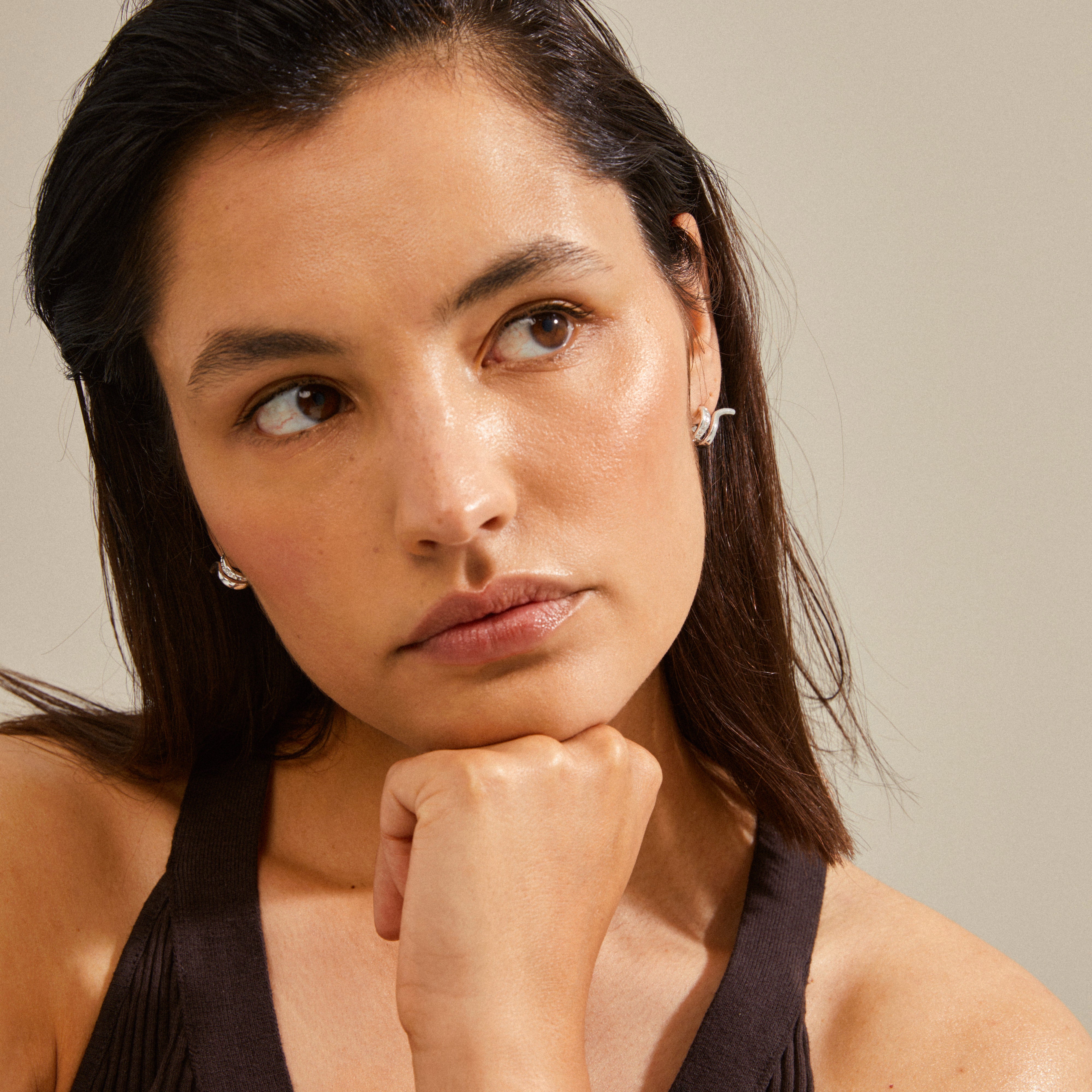 Woman wearing silver-plated NADINE earrings by Pilgrim, featuring small huggie hoops with an ear crawler effect and Preciosa crystals for a sophisticated look.