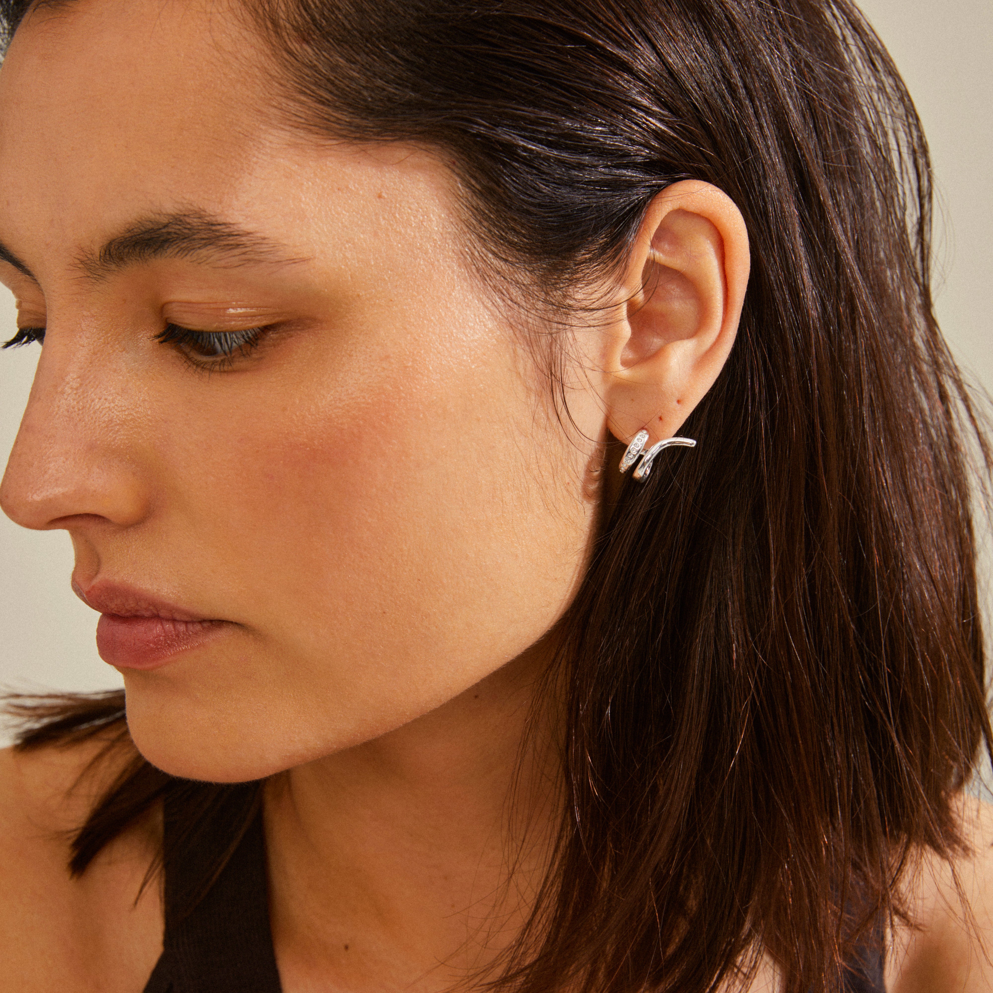 Close-up of a woman wearing silver-plated NADINE earrings from Pilgrim, showcasing their unique ear crawler design with shiny Preciosa crystals.