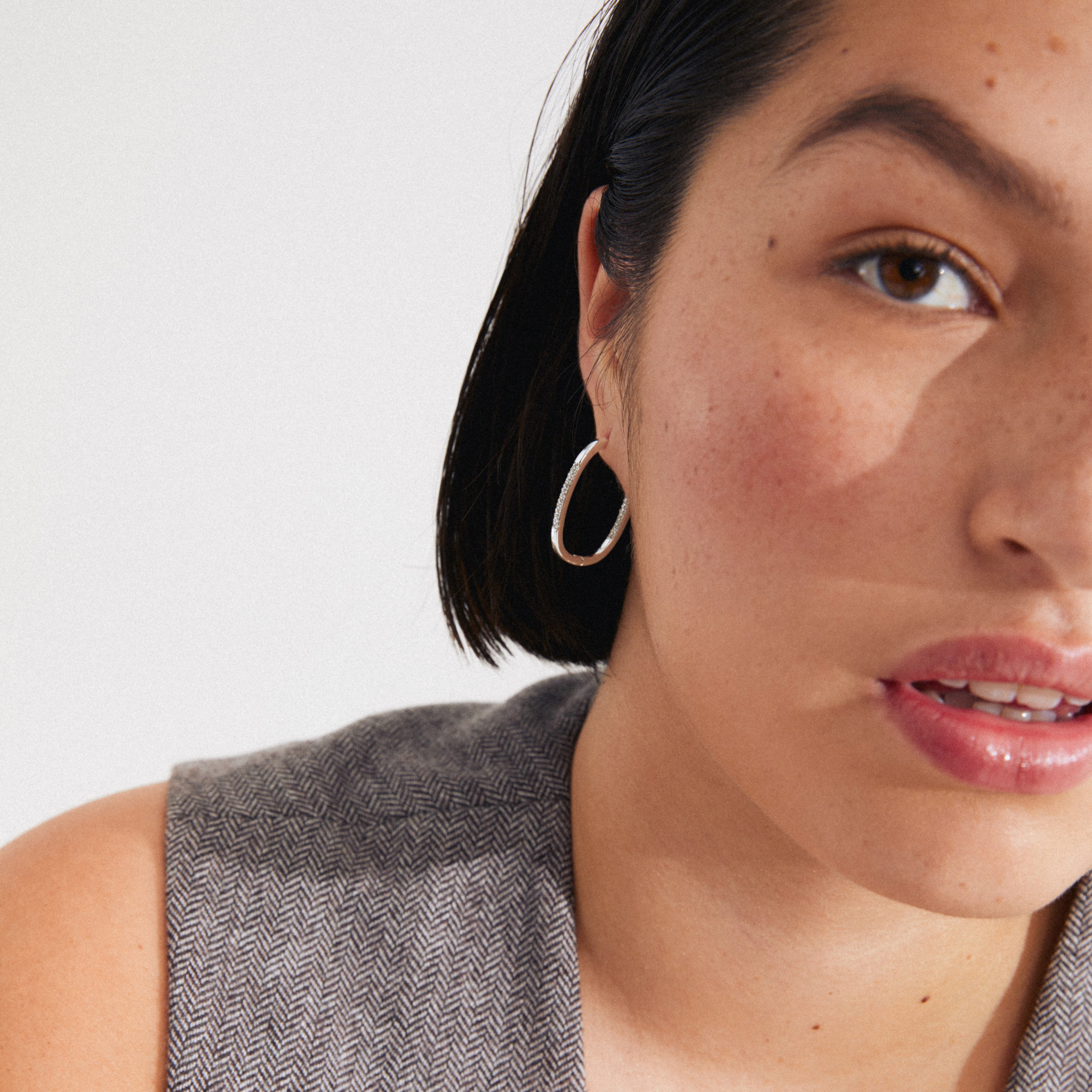 Silver-plated STAR hoops featuring oval design and sparkling Preciosa crystals, worn by a woman with dark hair, embodying Pilgrim's blend of timeless and trendy style.