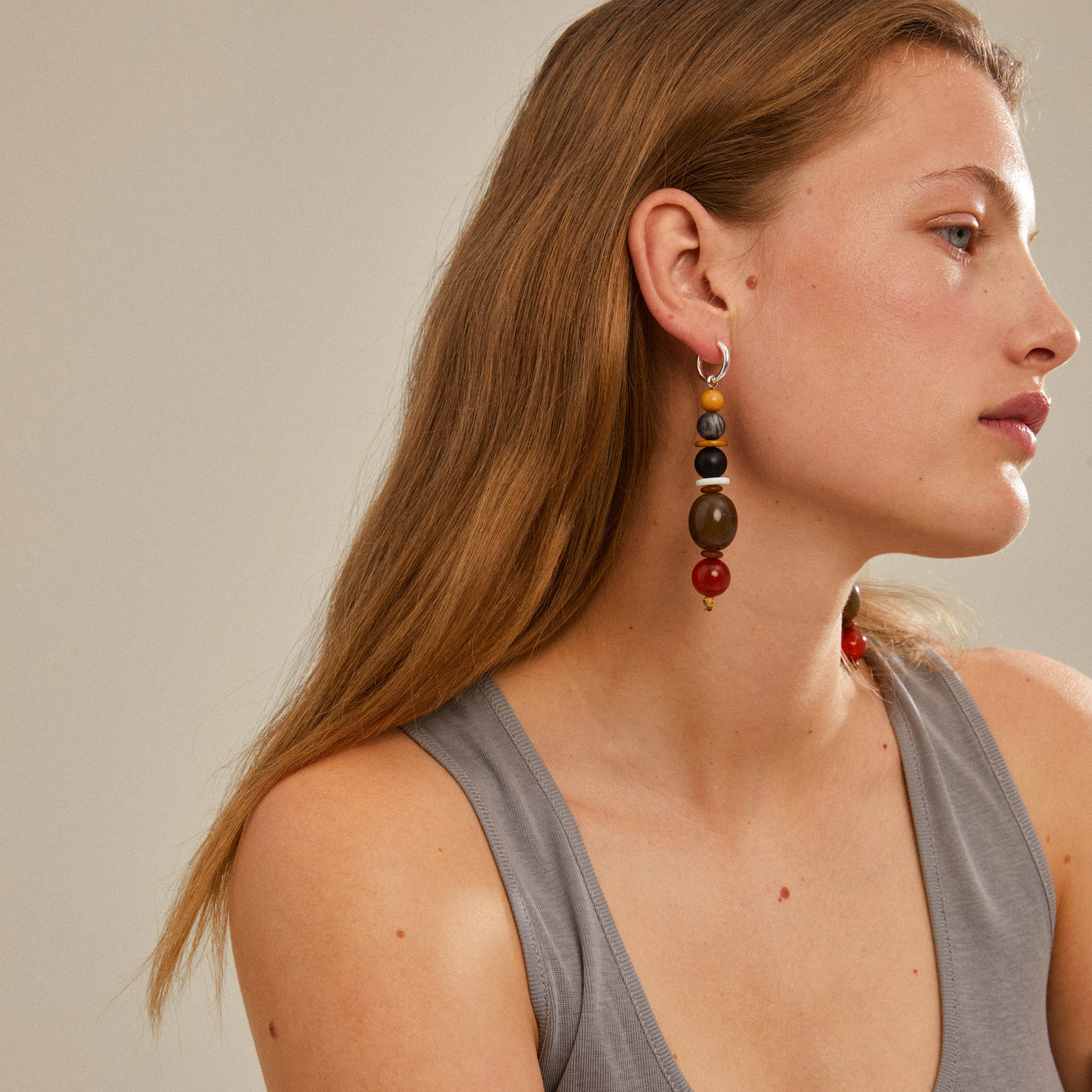 Woman wearing NAILA earrings, silver-plated hoops with dark earthy-toned beads from Pilgrim, showcasing a stylish, trendy accessory.
