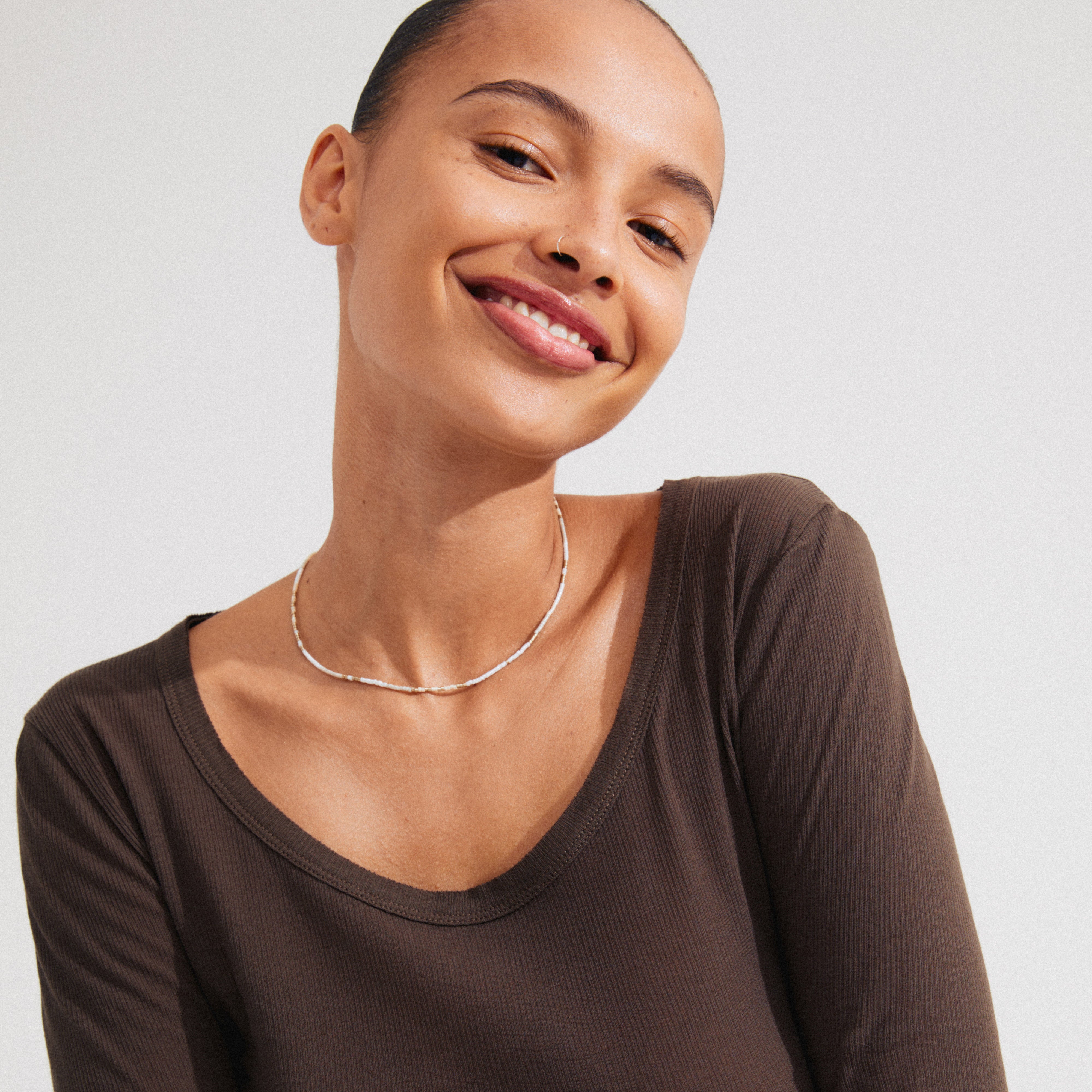 Woman wearing Pilgrim's ALISON necklace, featuring white and grey glass beads on a gold-plated chain, smiling warmly at the camera.