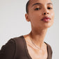 Woman wearing Pilgrim's ALISON necklace, featuring white and grey glass beads with a gold-plated chain, styled for a relaxed, boho-inspired look.