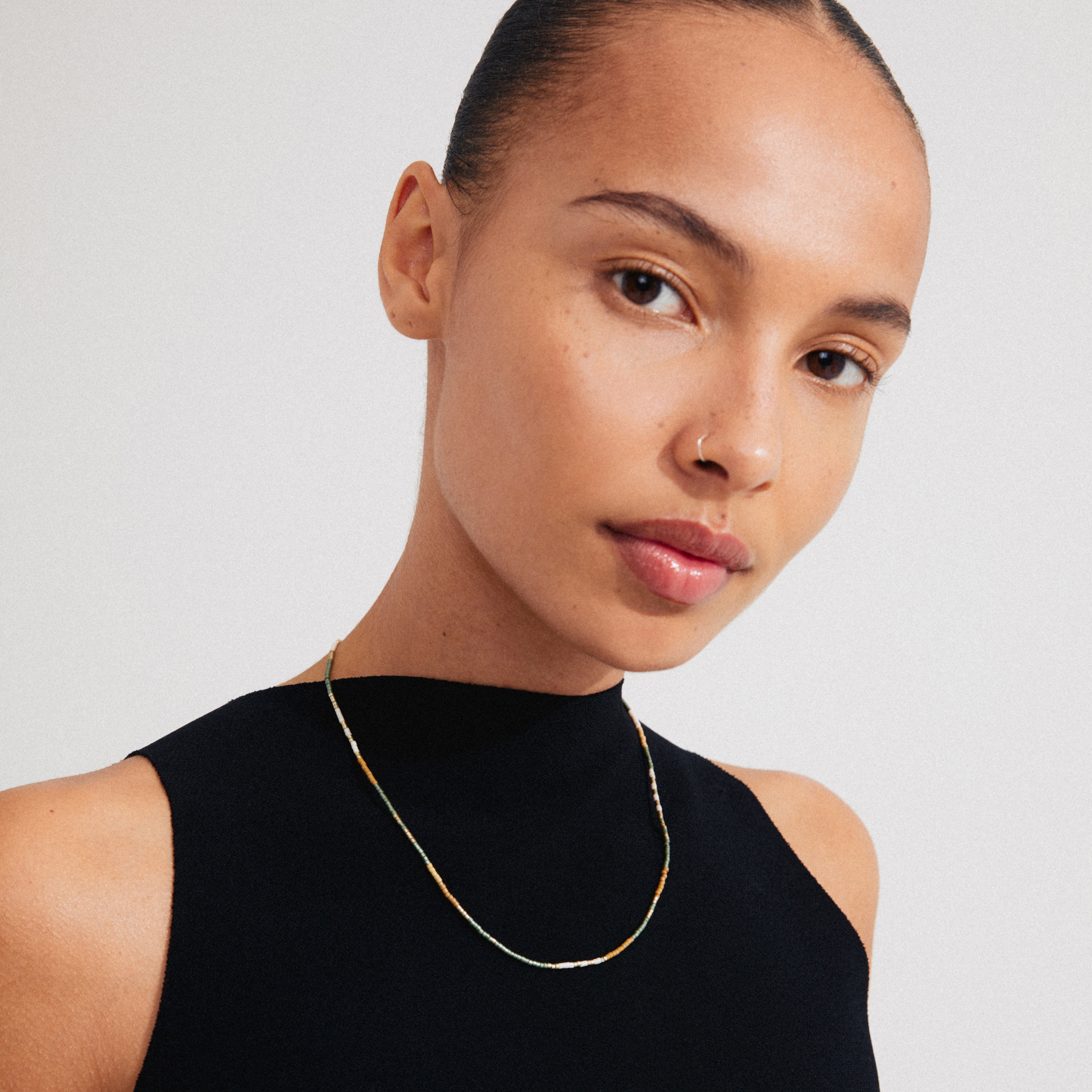 Woman wearing Pilgrim's ALISON necklace, featuring taupe and grey glass beads, styled close to the neck with a gold-plated extension chain.