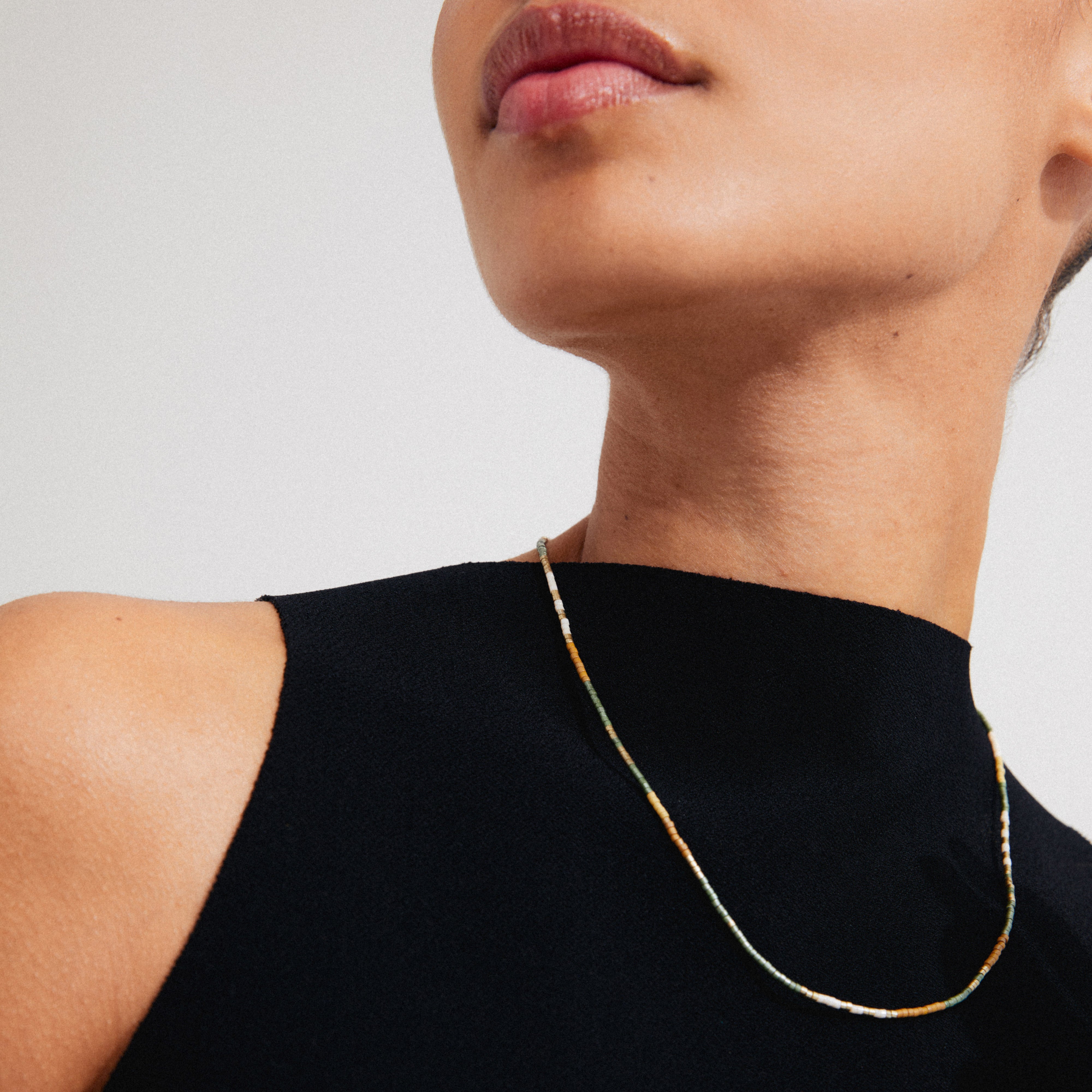 Woman wearing Pilgrim's ALISON necklace, a gold-plated chain with taupe and grey glass beads, styled close to the neck.