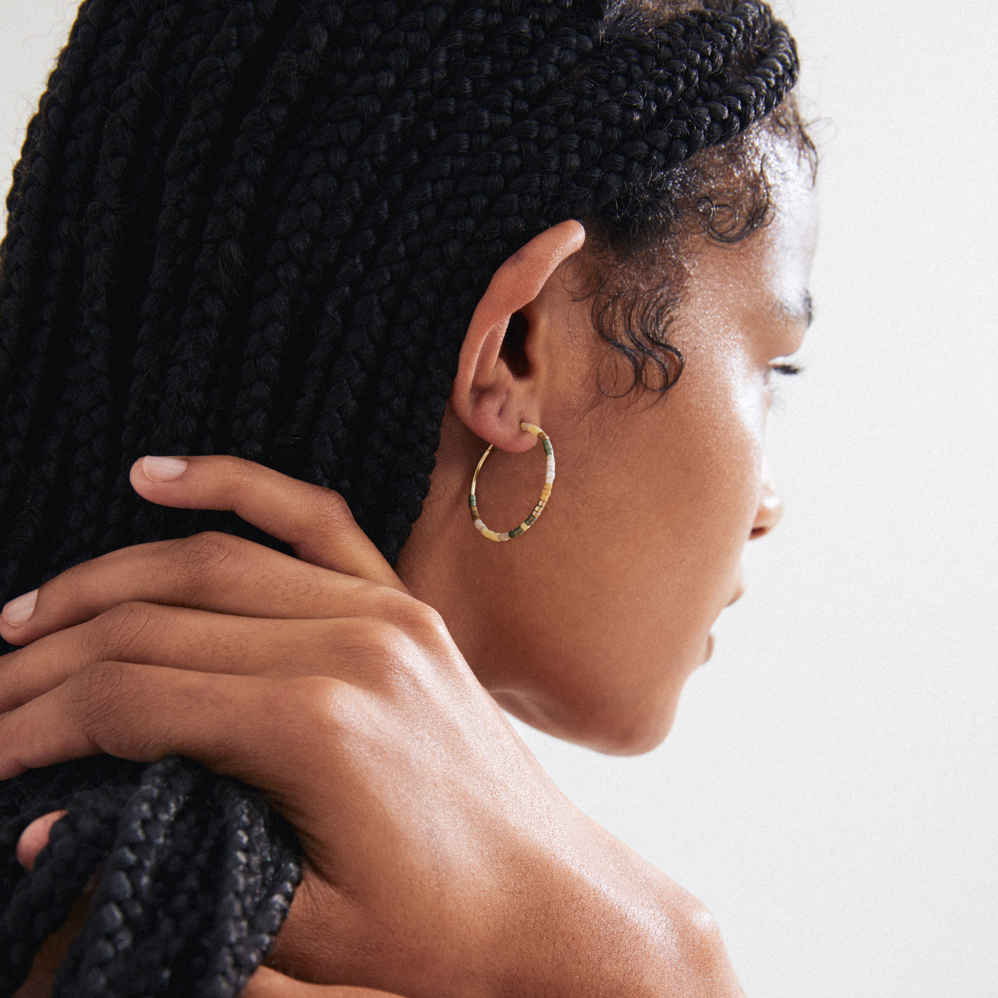 Woman with braids wearing Pilgrim's ALISON hoop earrings, showcasing gold-plated design with earthy glass beads, embodying a natural bohemian style.