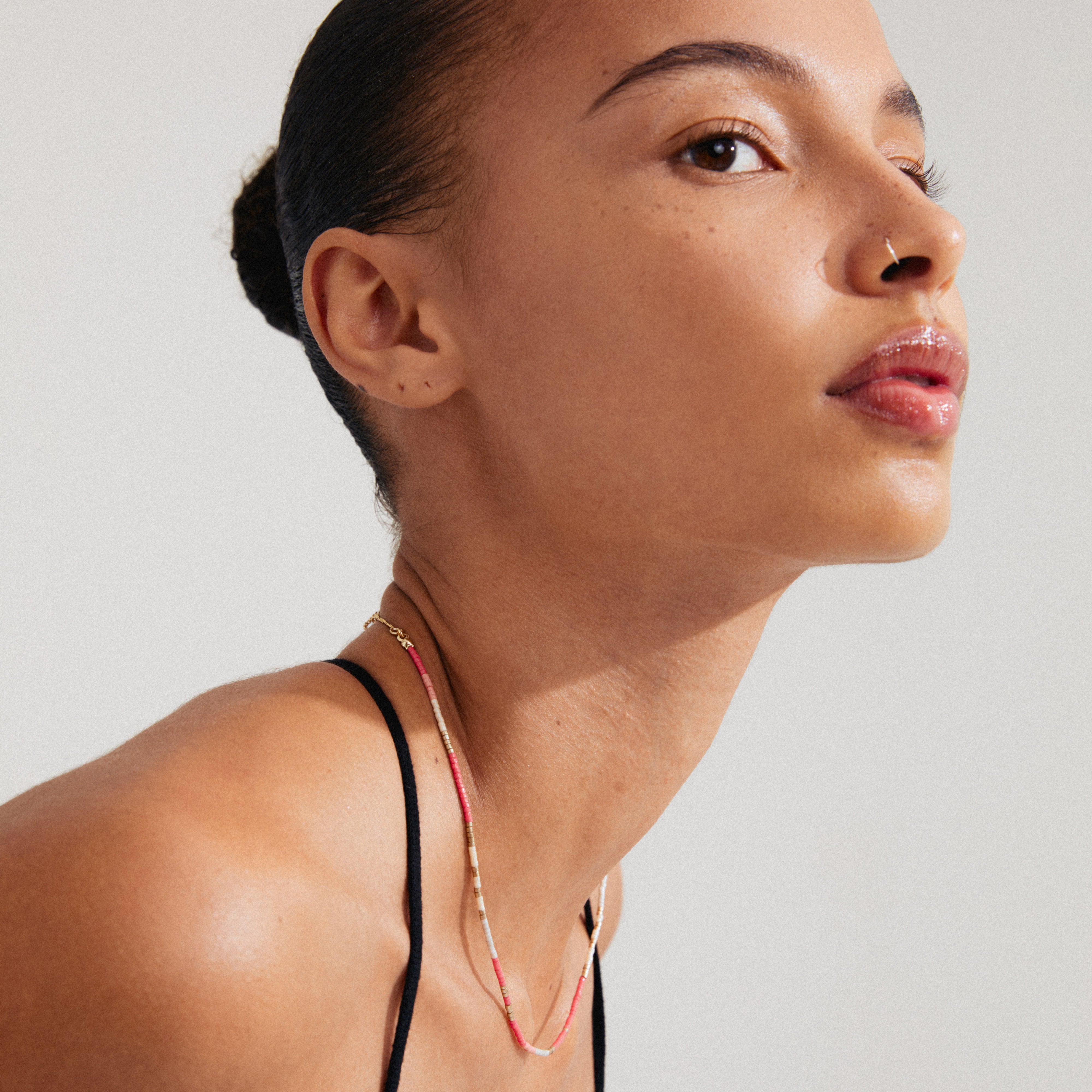 Close-up of a woman wearing Pilgrim's ALISON necklace, featuring pink and grey glass beads and a gold-plated chain for a boho-inspired layered look.