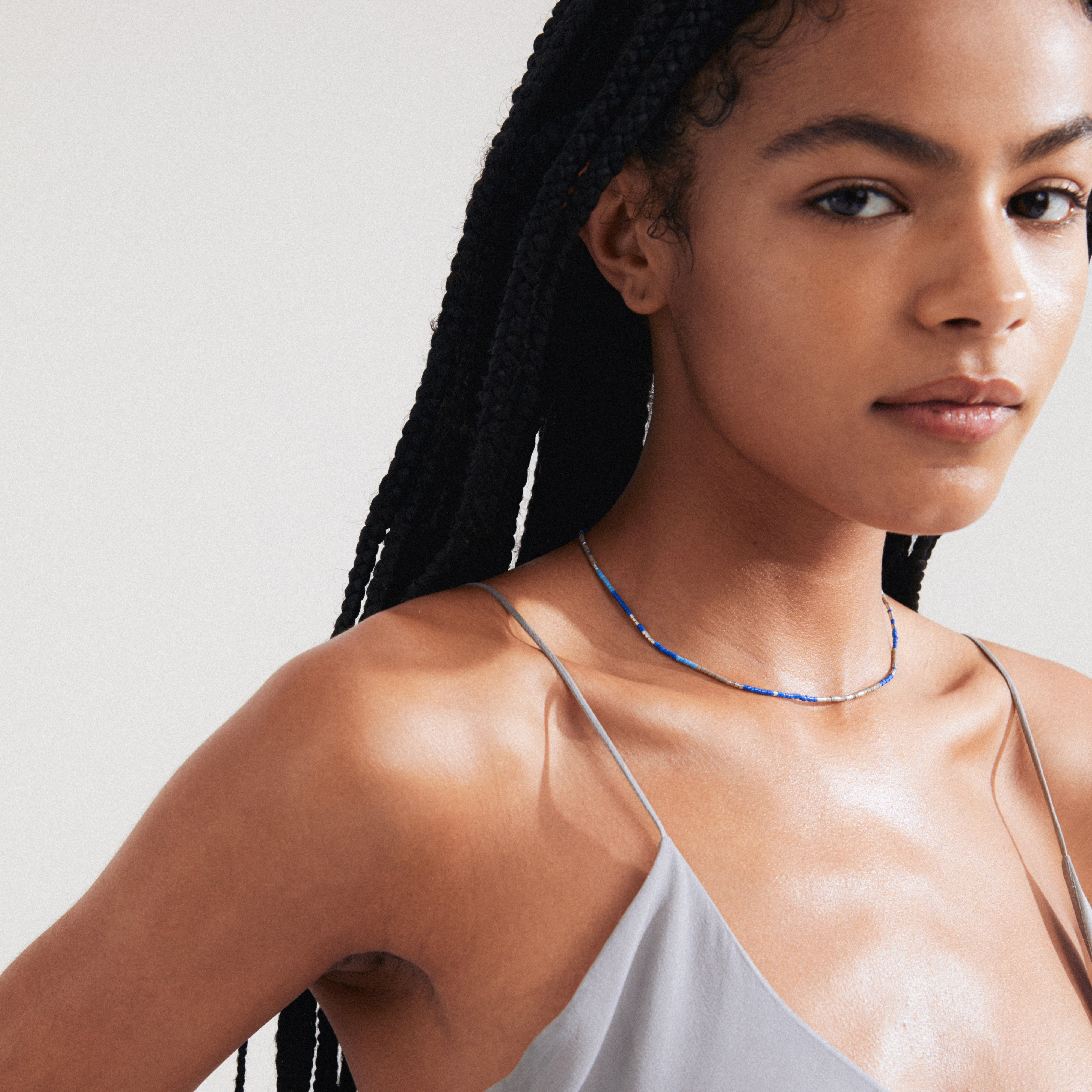 Woman with braids wearing the ALISON necklace, a blue, silver-plated piece from Pilgrim, styled for a relaxed, festival-inspired look.
