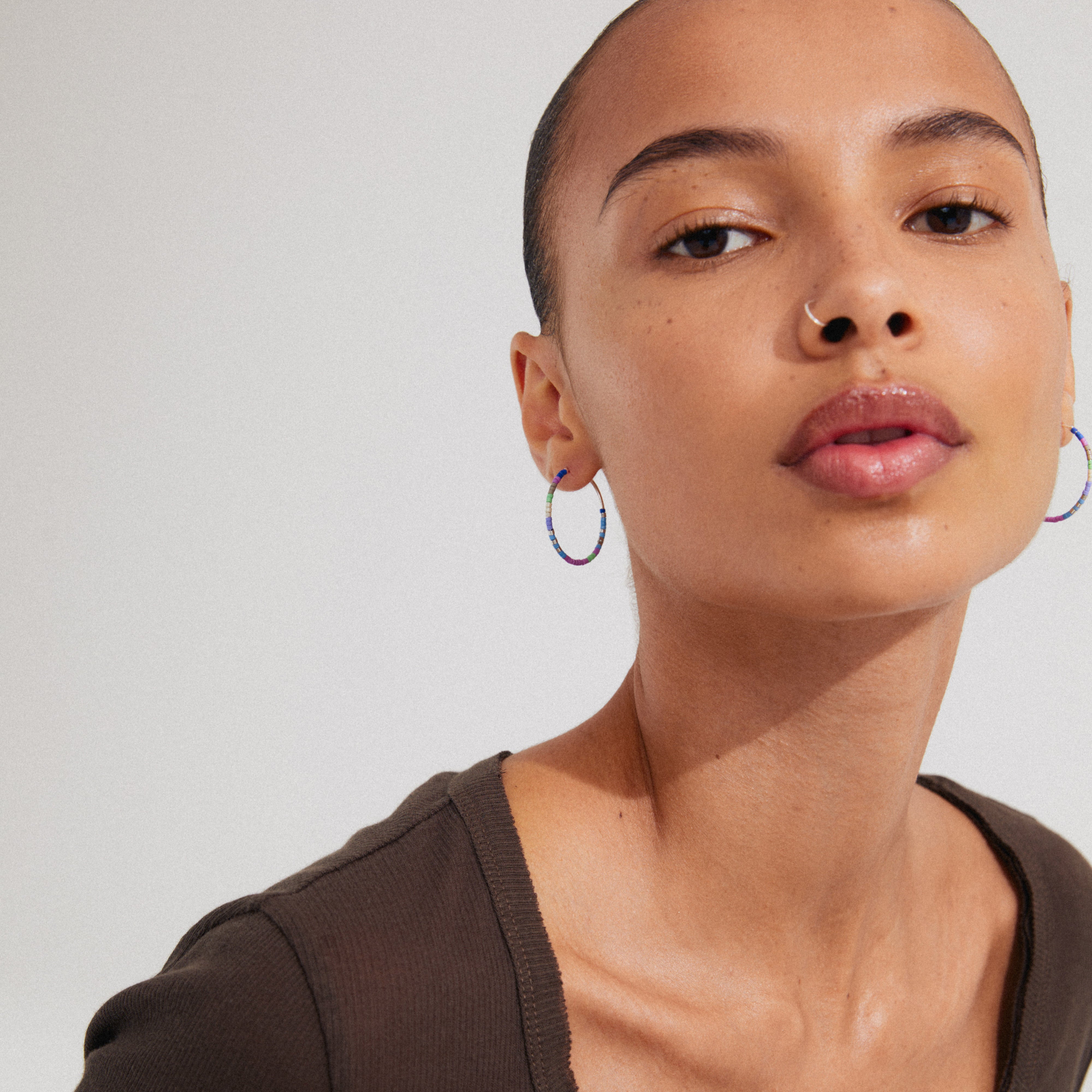 Woman showcasing Pilgrim's ALISON hoop earrings, featuring silver-plated hoops adorned with blue and purple glass beads.